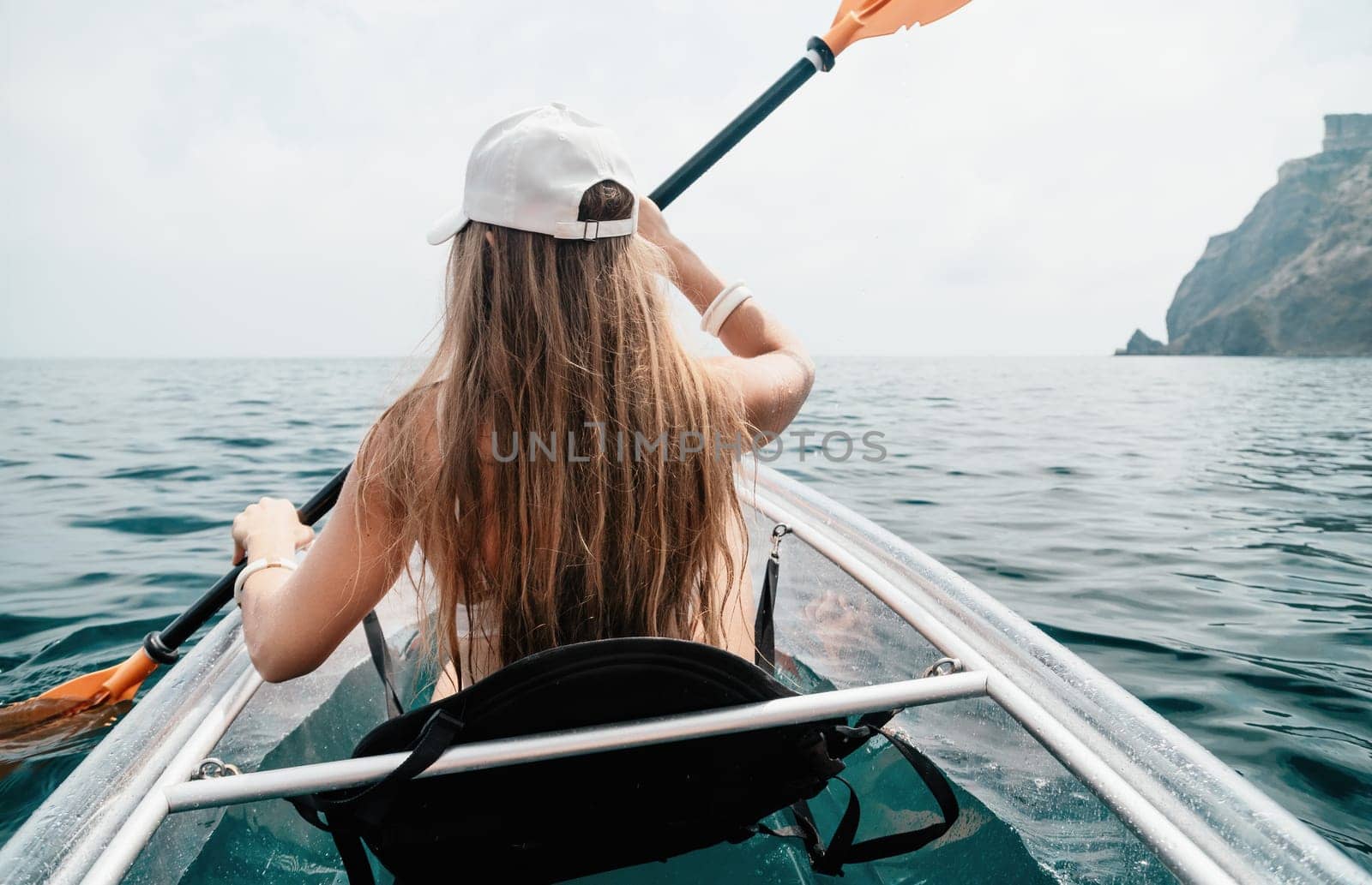 Woman in kayak back view. Happy young woman with long hair floating in transparent kayak on the crystal clear sea. Summer holiday vacation and cheerful female people having fun on the boat.