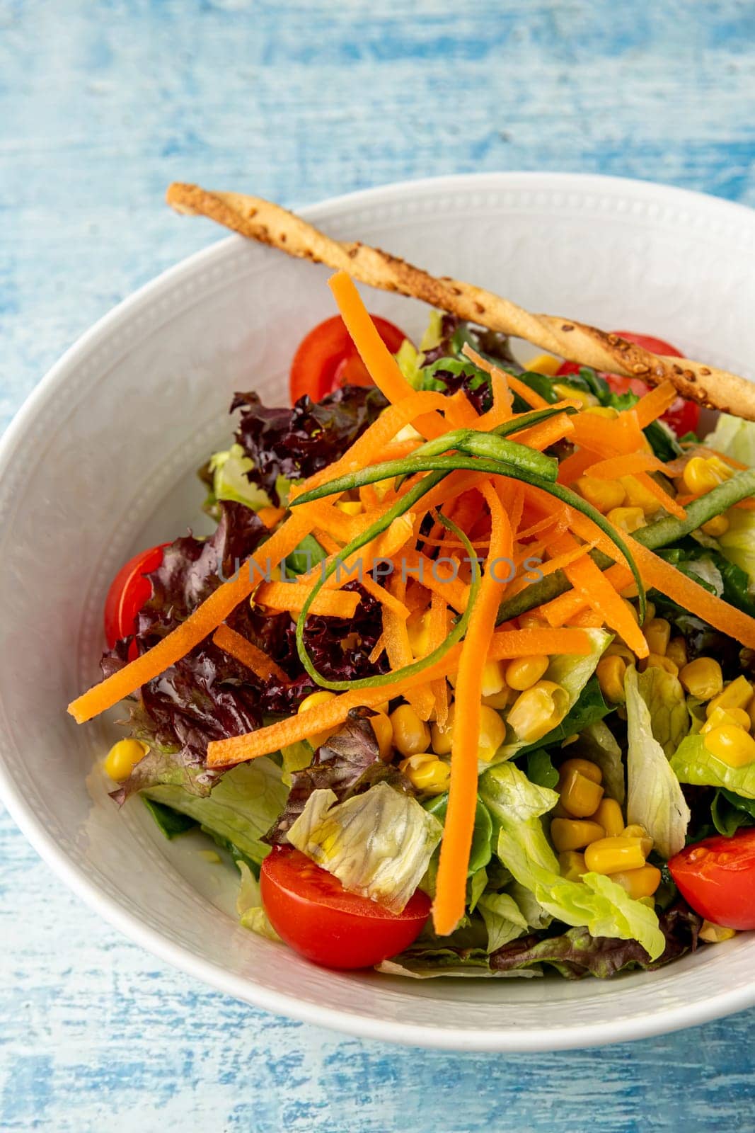 Healthy mixed salad in white bowl on wooden table. Mediterranean salad