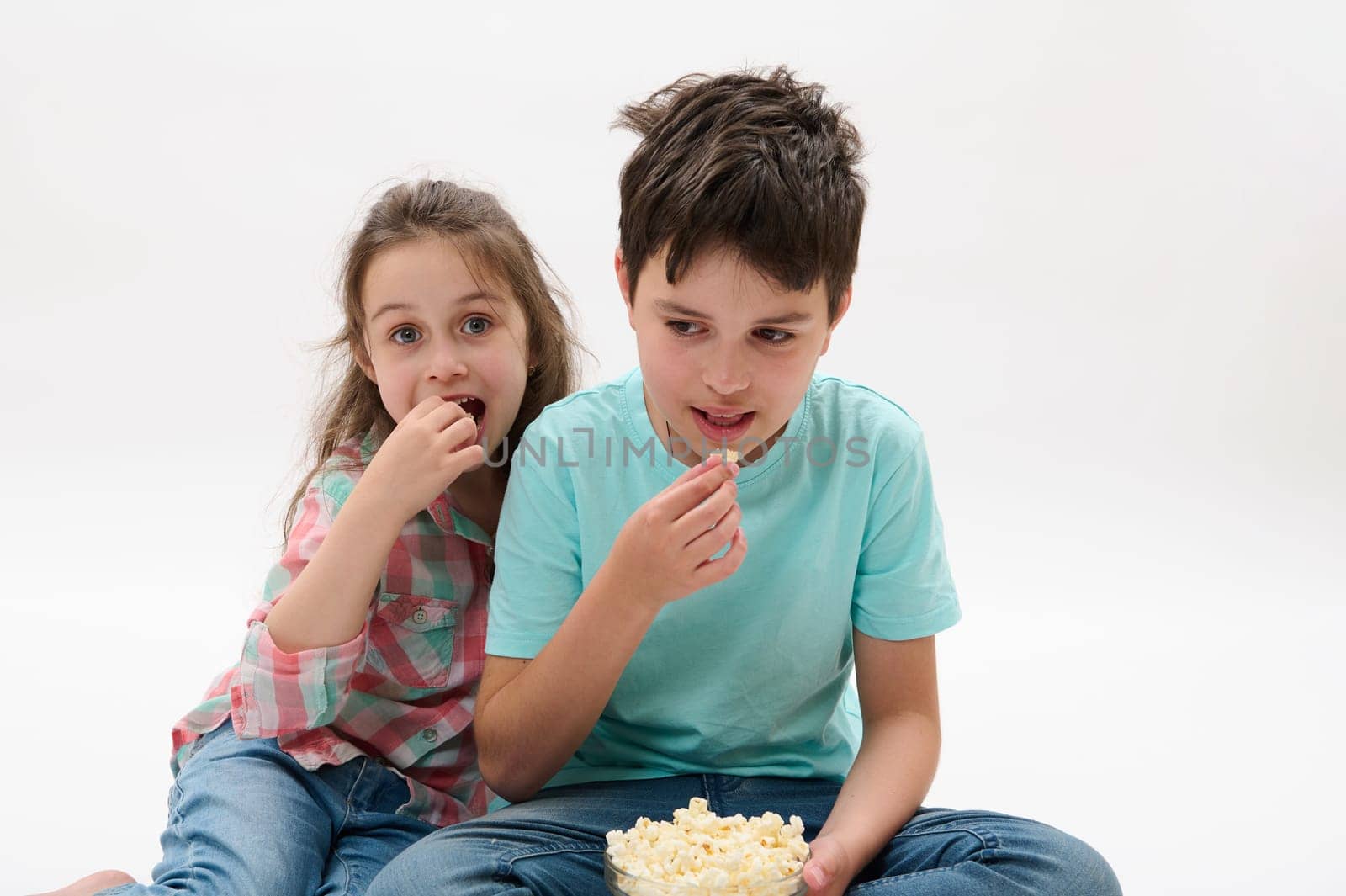 Happy kids, boy and girl eating popcorn, watching movie, smiling looking at camera, isolated on white studio background by artgf