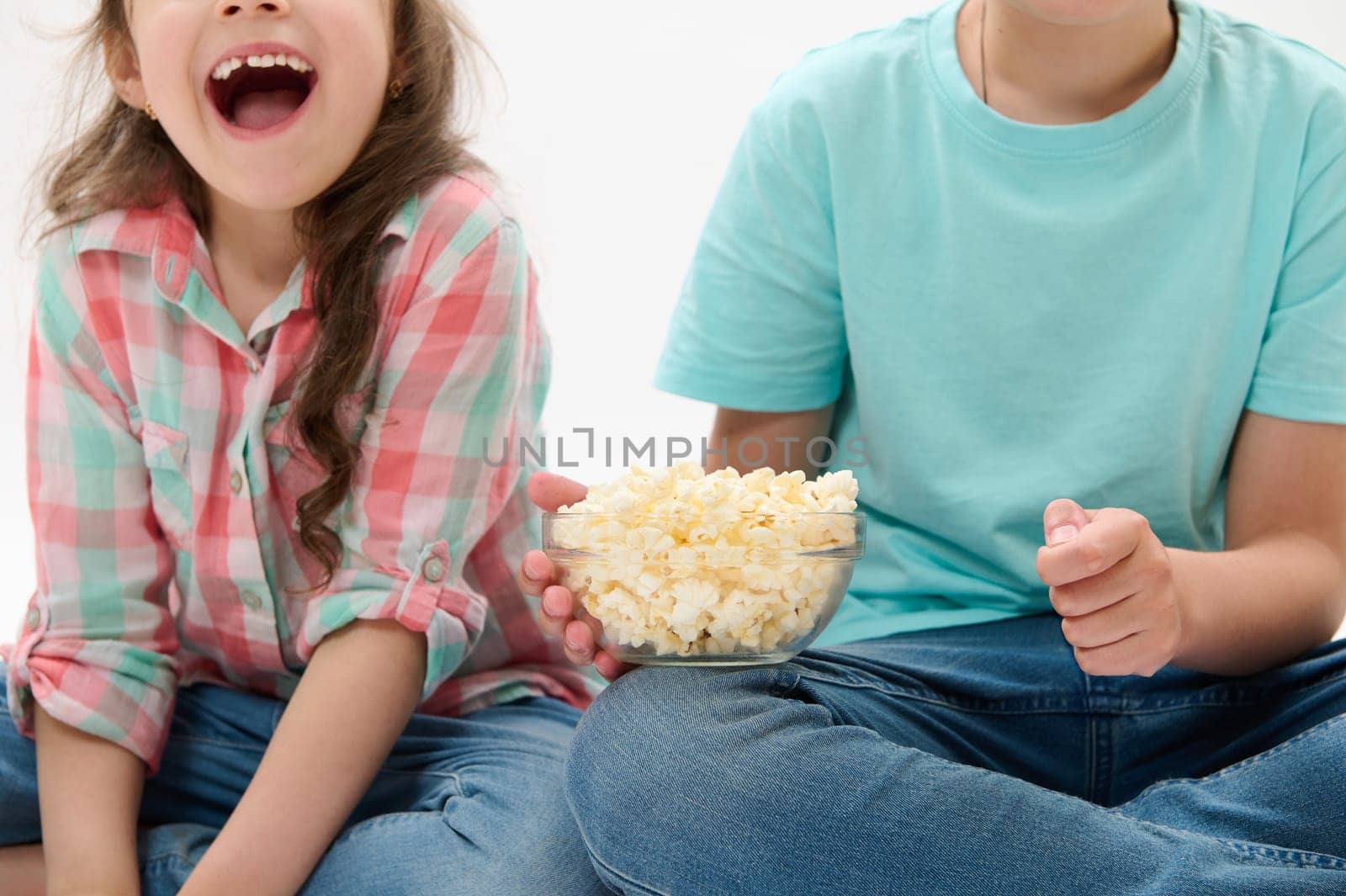 Details on a bowl of popcorn in the hands of cute cheery children watching movies or cartoons over white isolated background. People. Kids. Childhood. Lifestyle. Leisure activity. Entertainment