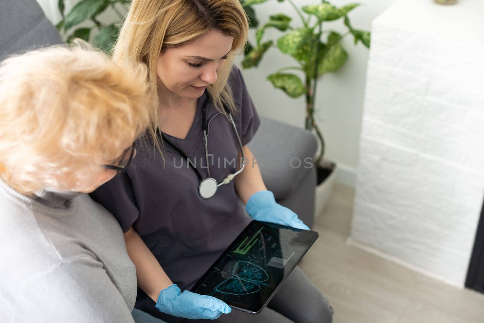 Serious GP doctor showing tablet screen to old 70s female patient, explaining electronic prescription, medical screening, examination result, giving consultation. Woman visiting practitioner