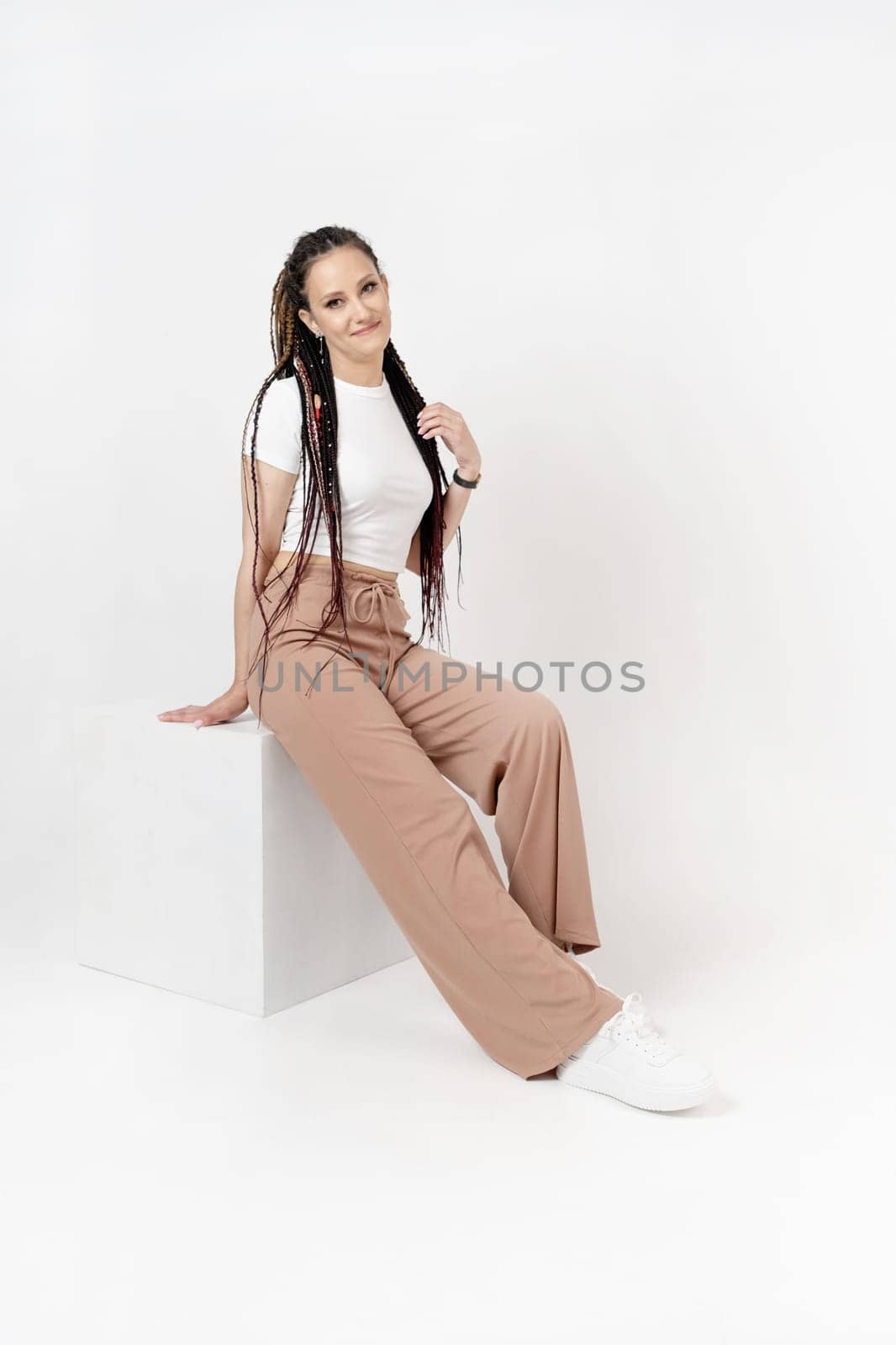 Fashionable young beautiful woman. Slim girl with dreadlocks in an active pose in a white pants and top. Fashion, clothing and style.