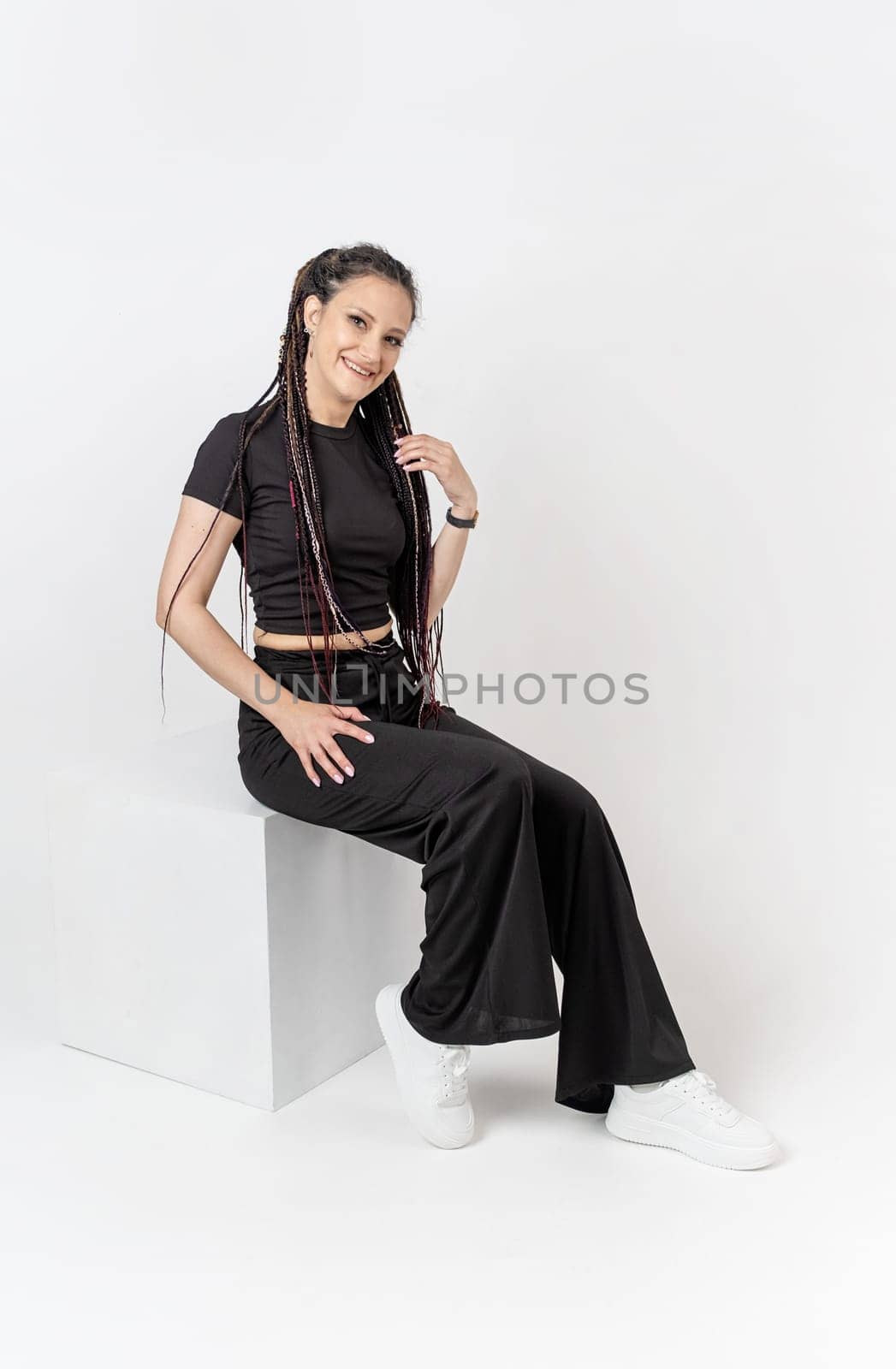 Fashionable young beautiful woman . Slim girl with dreadlocks in an active pose in black pants and top . Fashion, clothing and style.