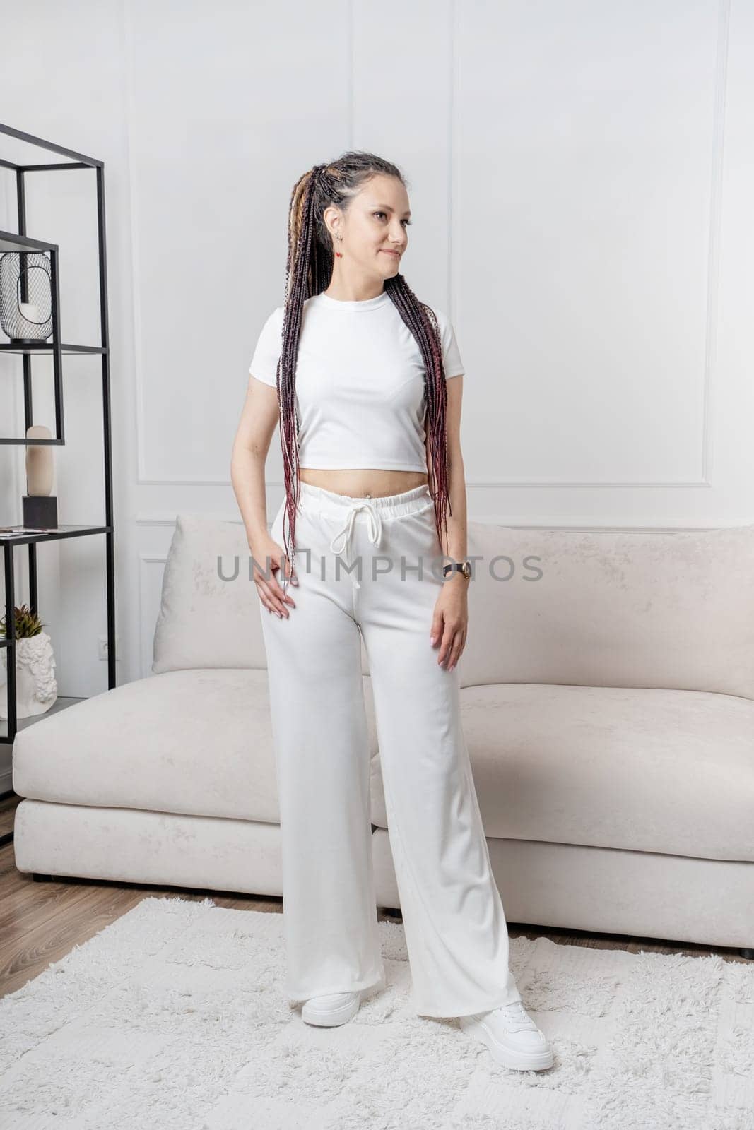 Fashionable young beautiful woman . Slim girl with dreadlocks in an active pose in a white pants and top . Fashion, clothing and style.