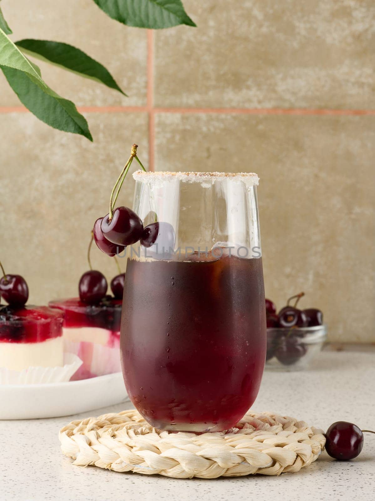 Cherry juice in a transparent glass and fresh cherries on a white table