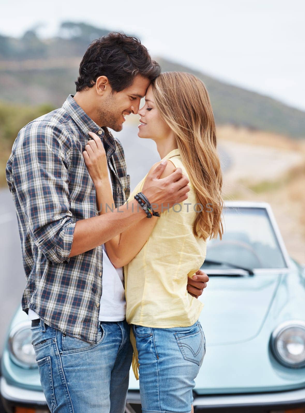 Going in for a kiss...An affectionate young couple standing alongside their convertible while on a roadtrip. by YuriArcurs