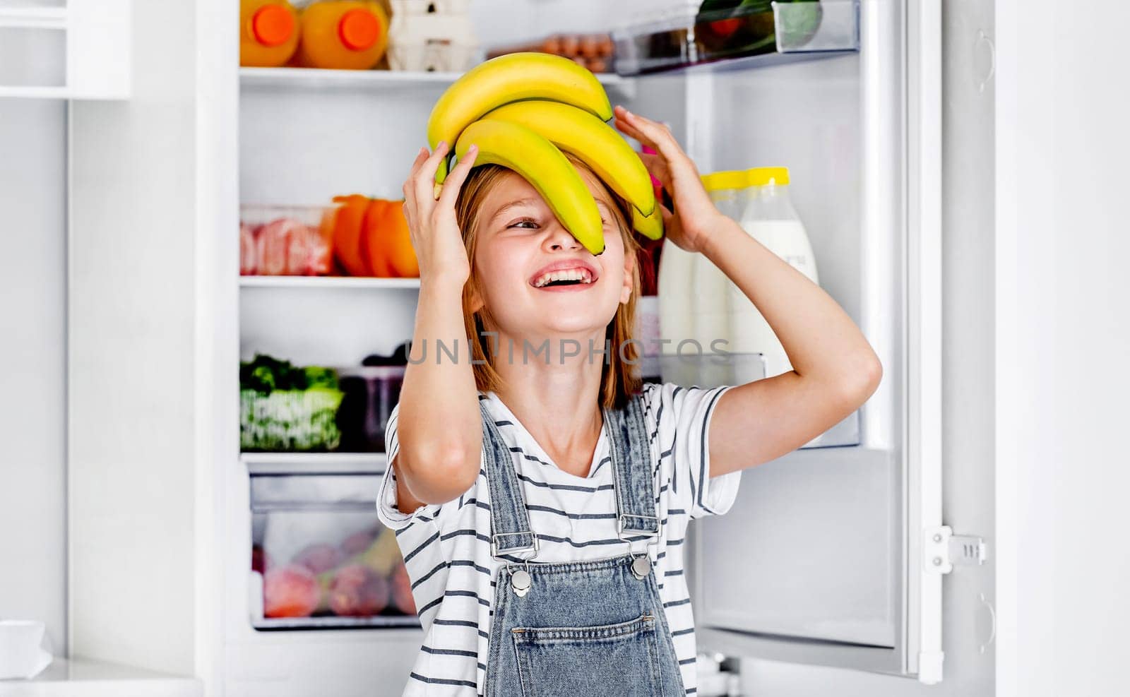 Preteen girl with bananas vitamin healthy food at kitchen. Pretty child kid enjoying yellow fruits at home
