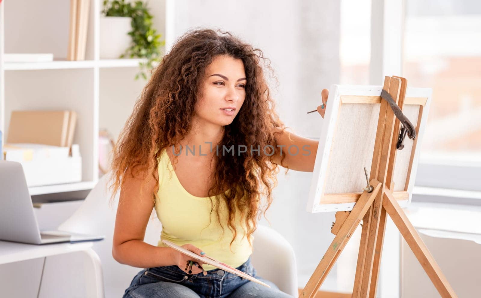 Beautiful girl painting picture on easel in light room