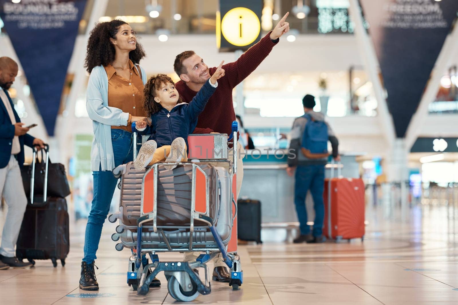 Pointing, travel and interracial family at the airport looking at a departure time for a flight. Happy, trip and parents with a child to look at information for arrival or leaving of an airplane by YuriArcurs