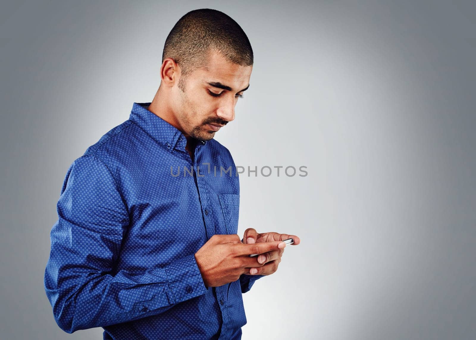 I keep my clients satisfied. Studio shot of a young businessman using his cellphone against a grey background. by YuriArcurs