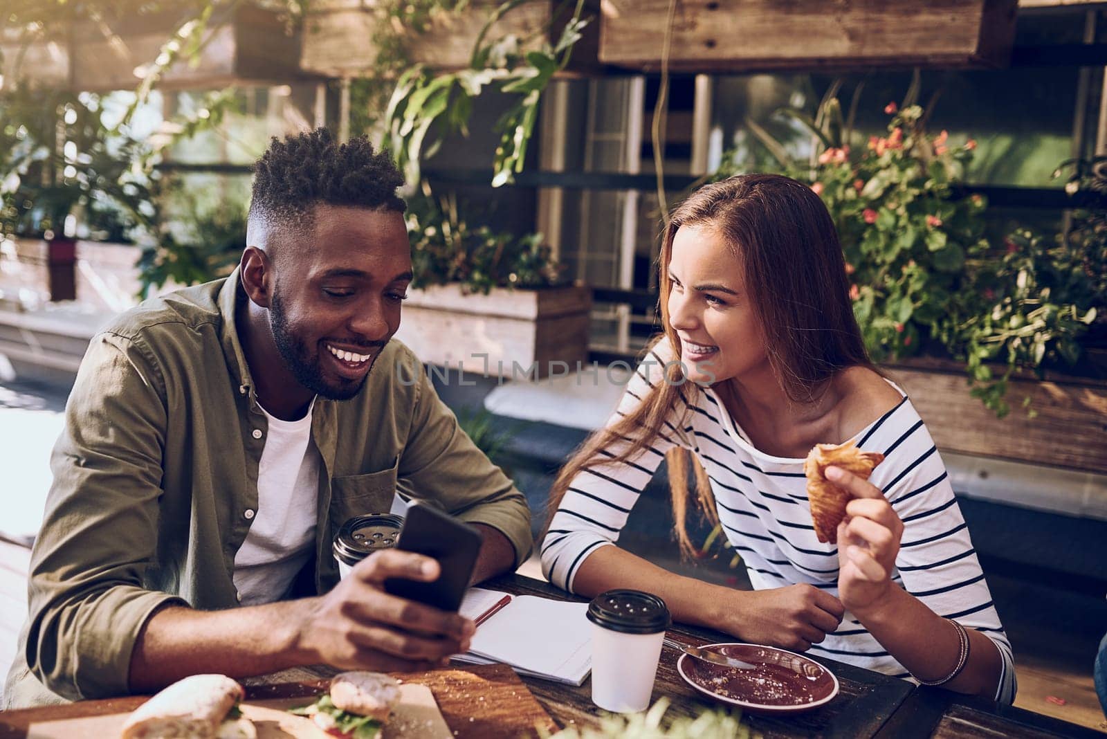 Restaurant, happy and friends laugh with phone for social media, mobile app and online website. Coffee shop, communication and black man and woman bonding on smartphone for meme, humor and internet by YuriArcurs