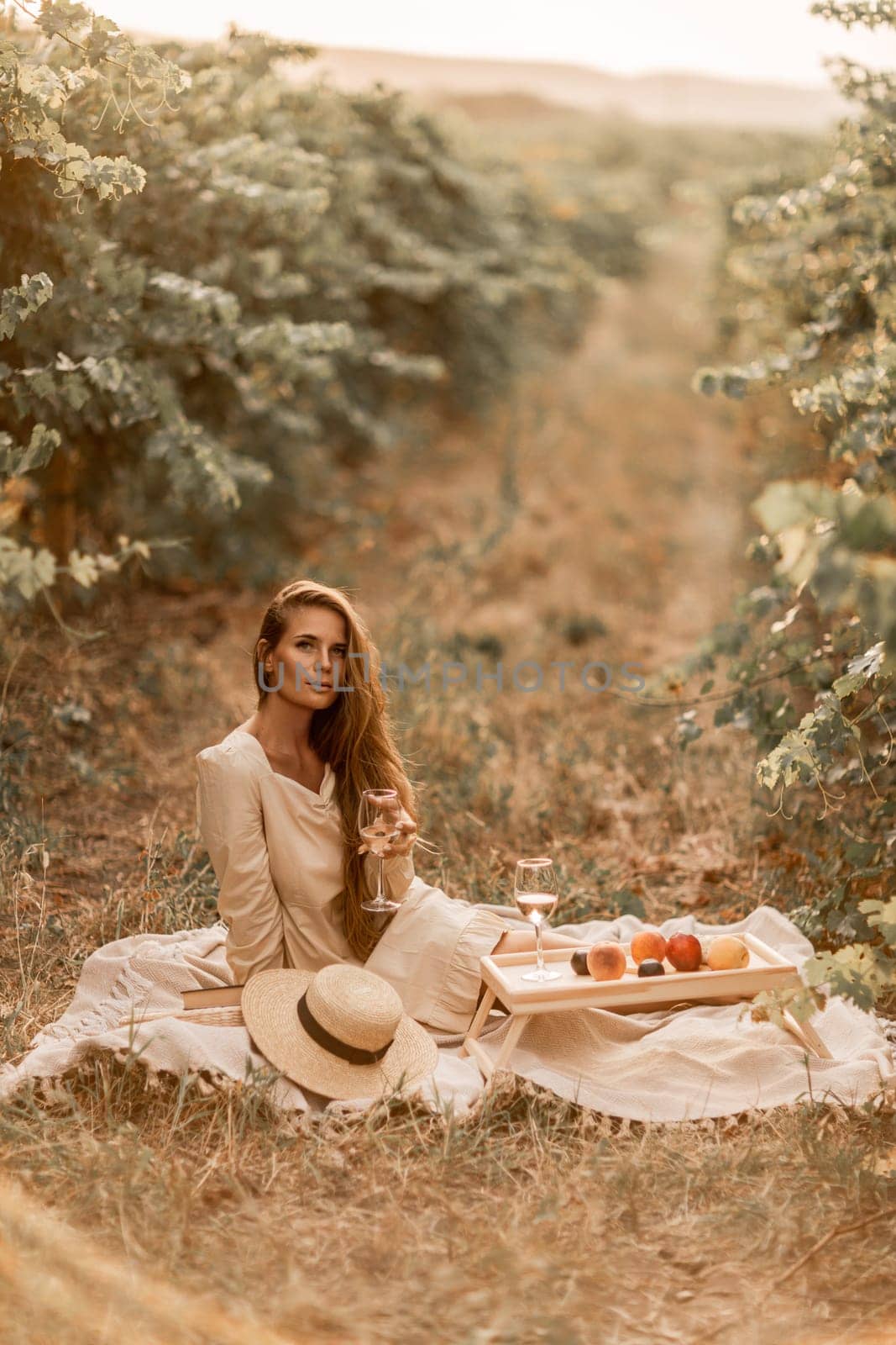 Woman picnic vineyard. Romantic dinner, fruit and wine. Happy woman with a glass of wine at a picnic in the vineyard on sunny day, wine tasting at sunset