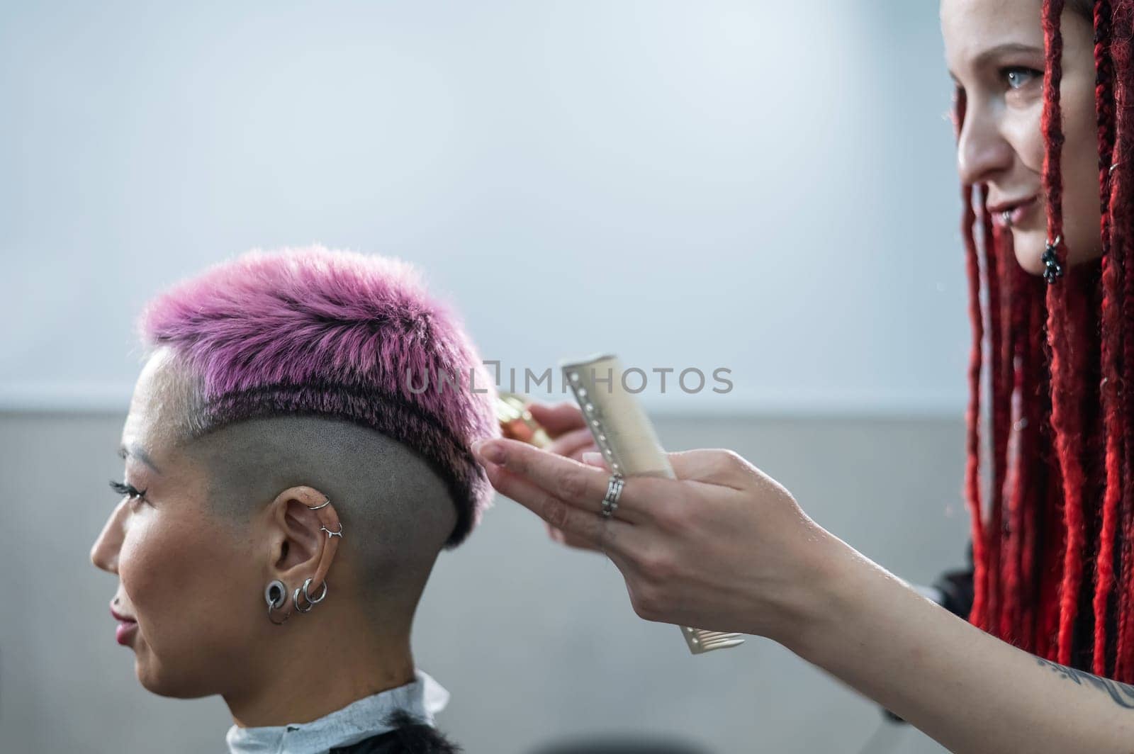Hairdresser cuts Asian woman with short pink hair in barbershop