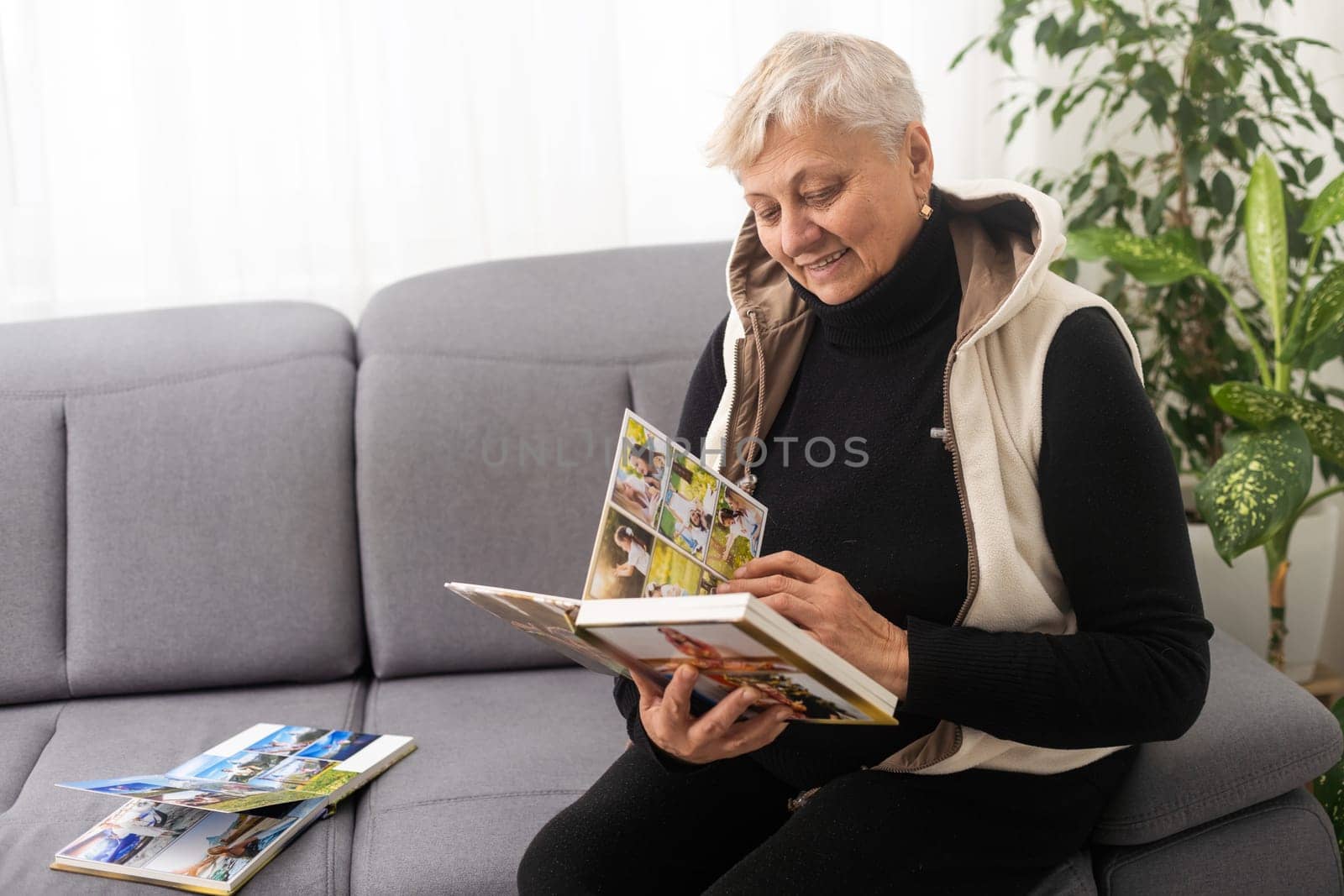 An elderly woman with nostalgia looks at old photos in a photo album or photobook - The concept of family and life values and loneliness in old age. by Andelov13