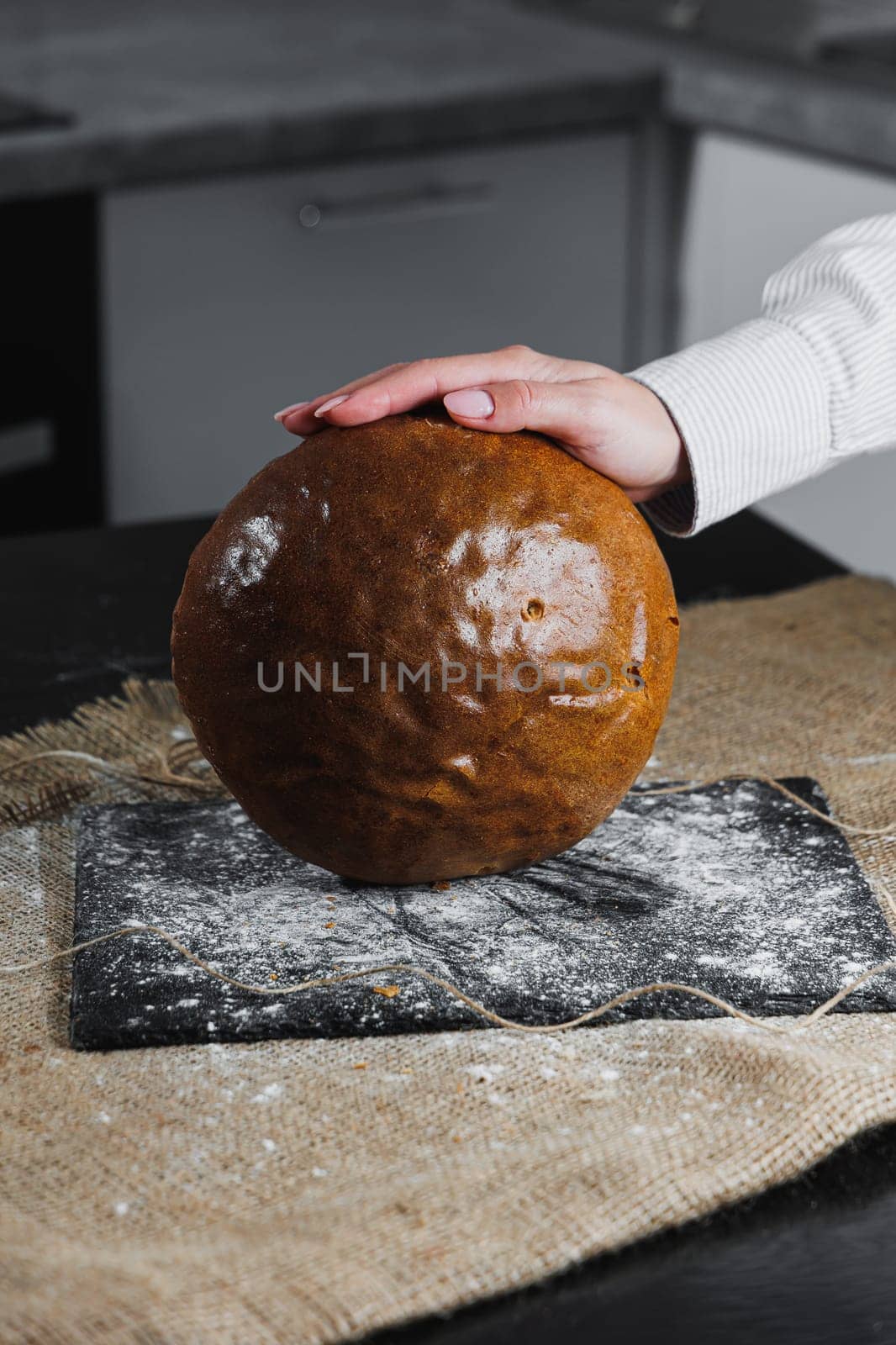 Homemade crispy loaf of bread. Baker holds fresh bread in his hands. Dark background