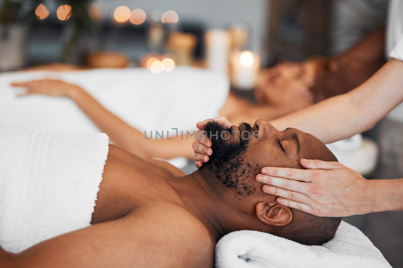 Spa, couple and massage for health and wellness at luxury resort for peace, calm and quiet time with hands of therapist in a beauty salon. Black man lying on bed for body, mind and head care at hotel by YuriArcurs