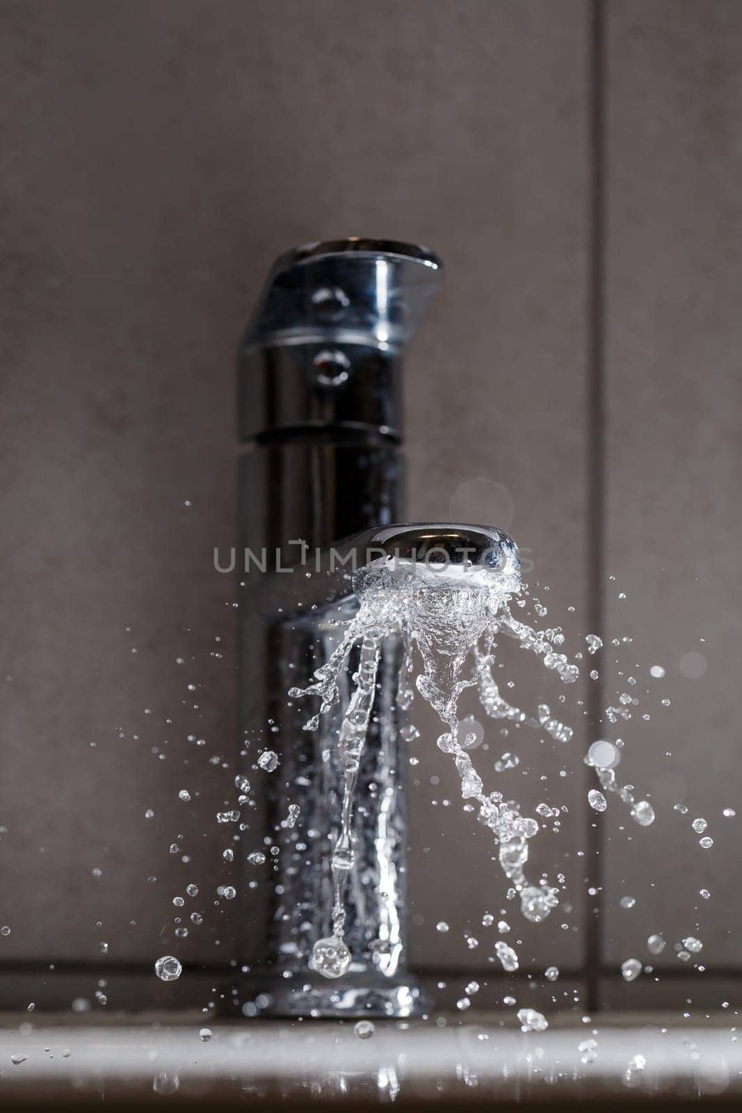 Broken water faucet in the bathroom sink. Water splashes from the silver faucet. Selective focus