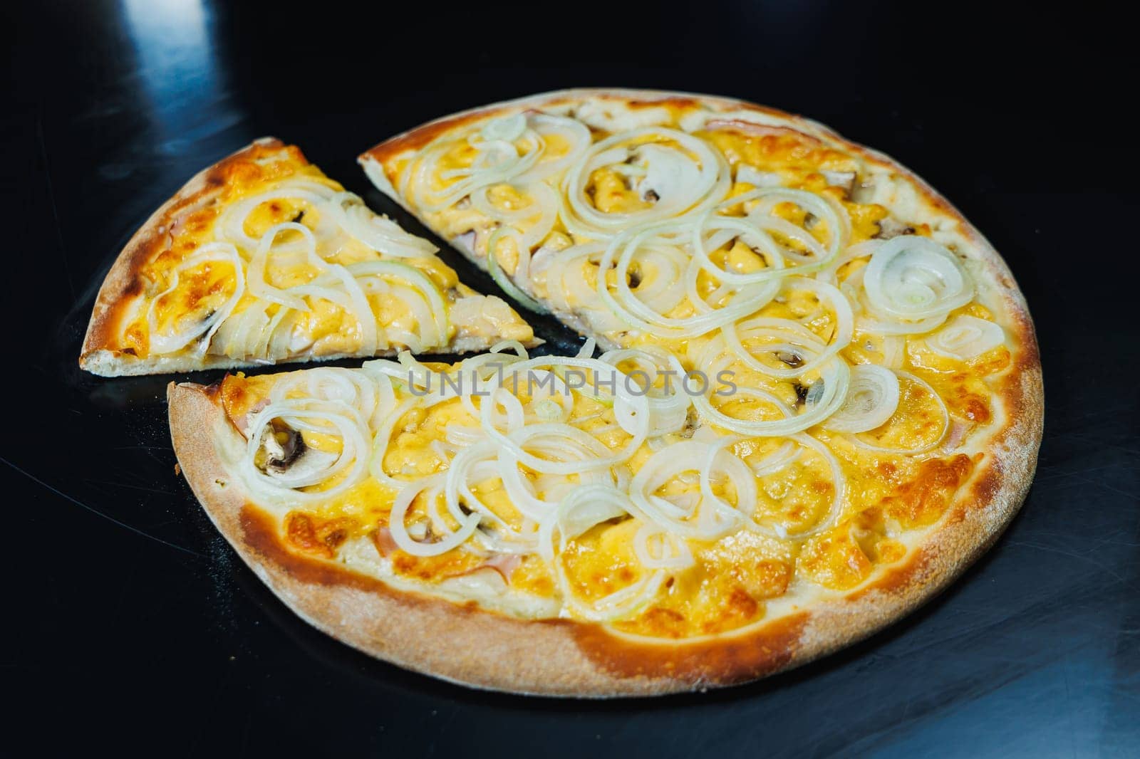 Sliced pizza with onion and meat, tomato sauce, mozzarella, onion and edge of dough, filled with cream cheese on a black background