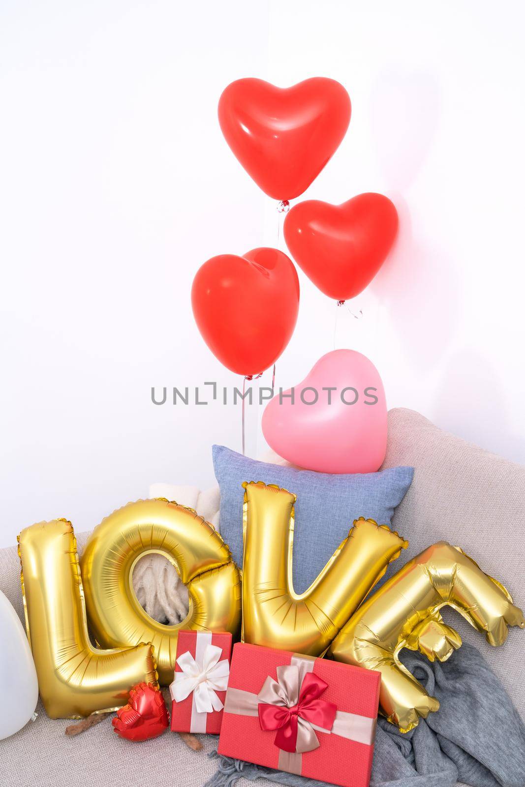 Foil love balloons and gifts on a sofa with white wall in background for Valentine's day, Mother's day surprise design concept.