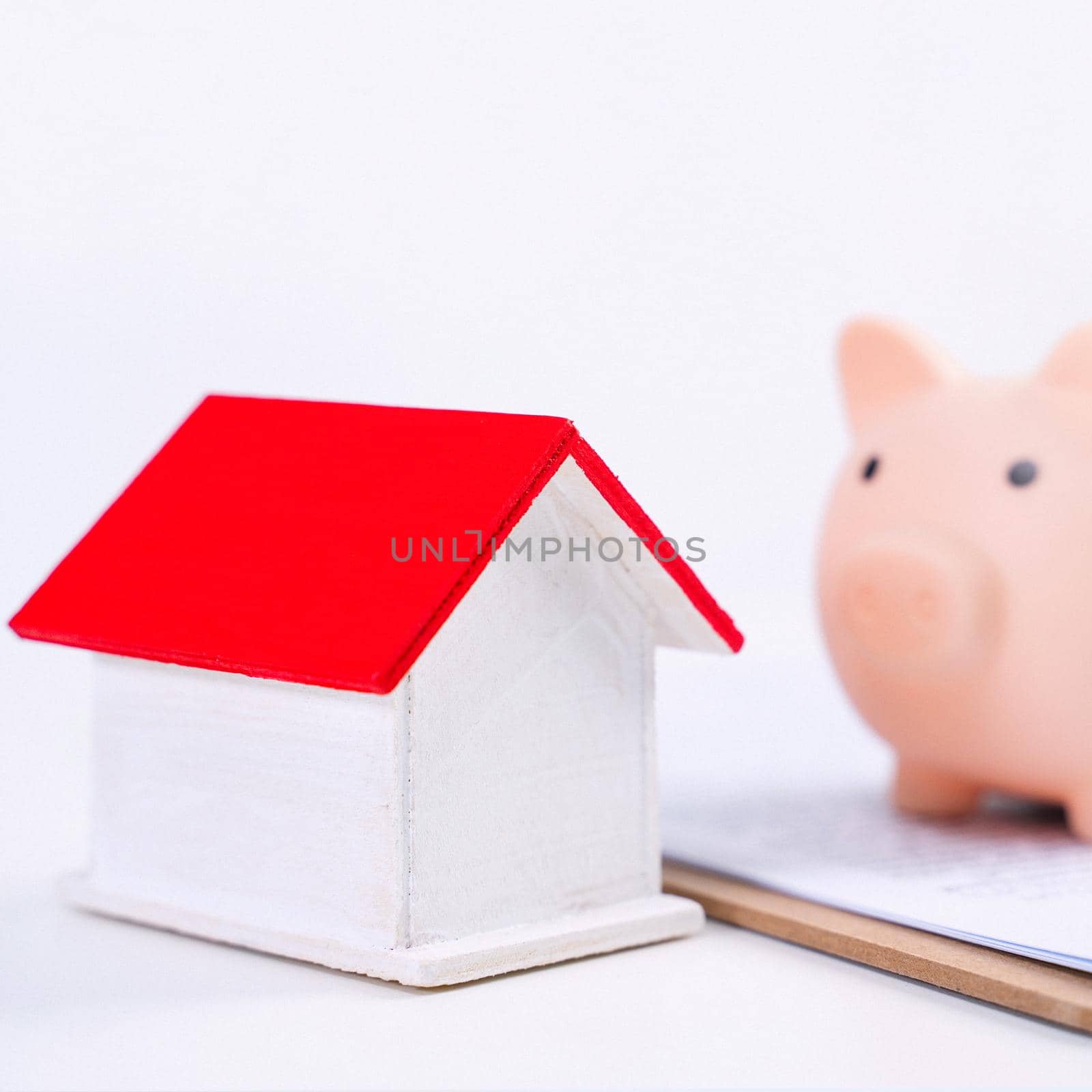 Financial concpet - Piggy bank, beautiful red white wooden house model on white background, saving money to buy insurance, close up, copy space. by ROMIXIMAGE