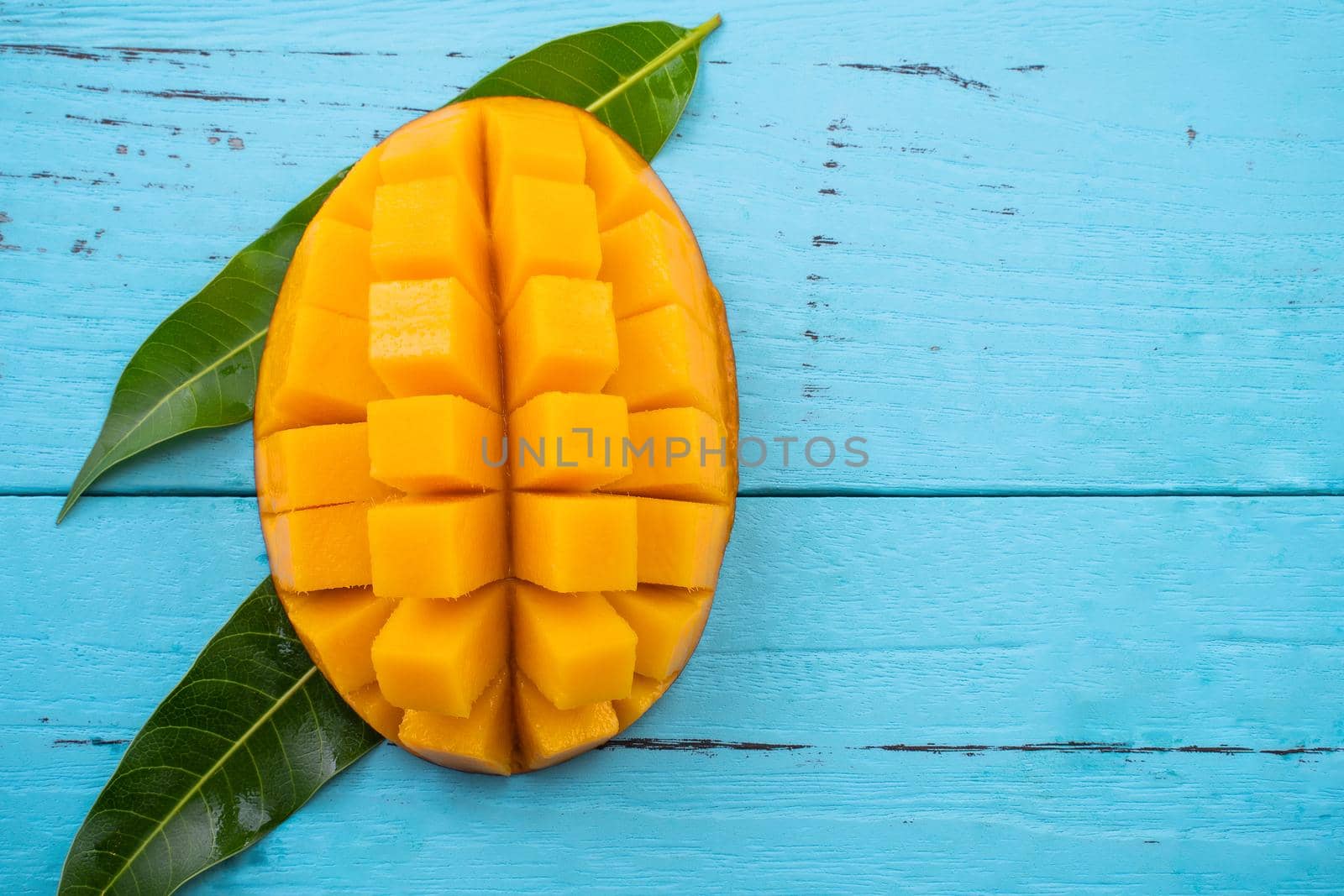 Mango - Fresh chopped tropical mango fruit isolated on bright vibrant light blue wooden table background, top view, flat lay layout, overhead shot.