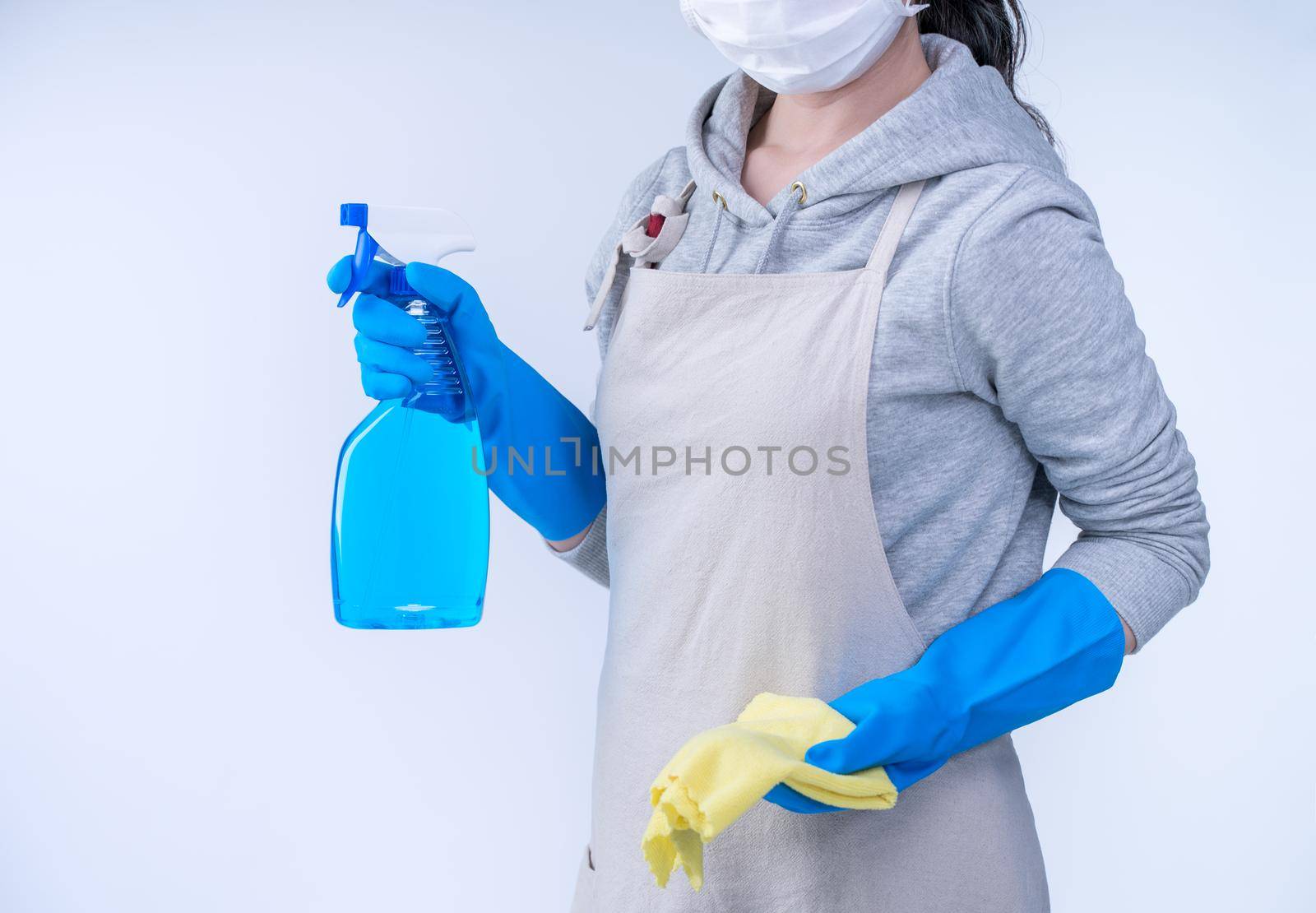 Young woman housekeeper in apron is doing cleaning with blue gloves, wet yellow rag, spraying bottle cleaner, close up, copy space, blank design concept. by ROMIXIMAGE