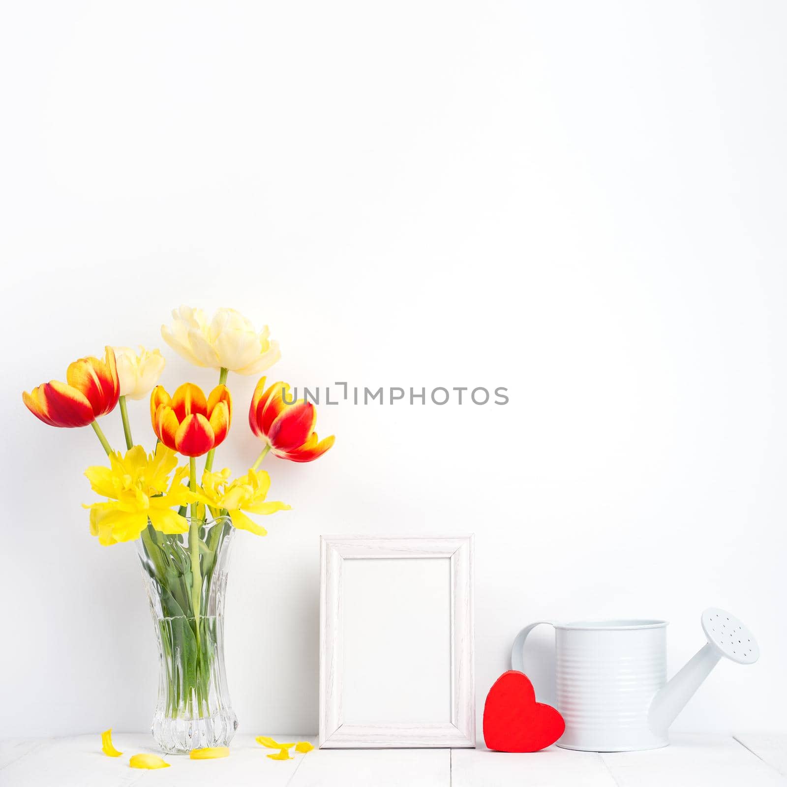 Tulip flower in glass vase with picture frame place on white wooden table background against clean wall at home, close up, Mother's Day decor concept. by ROMIXIMAGE
