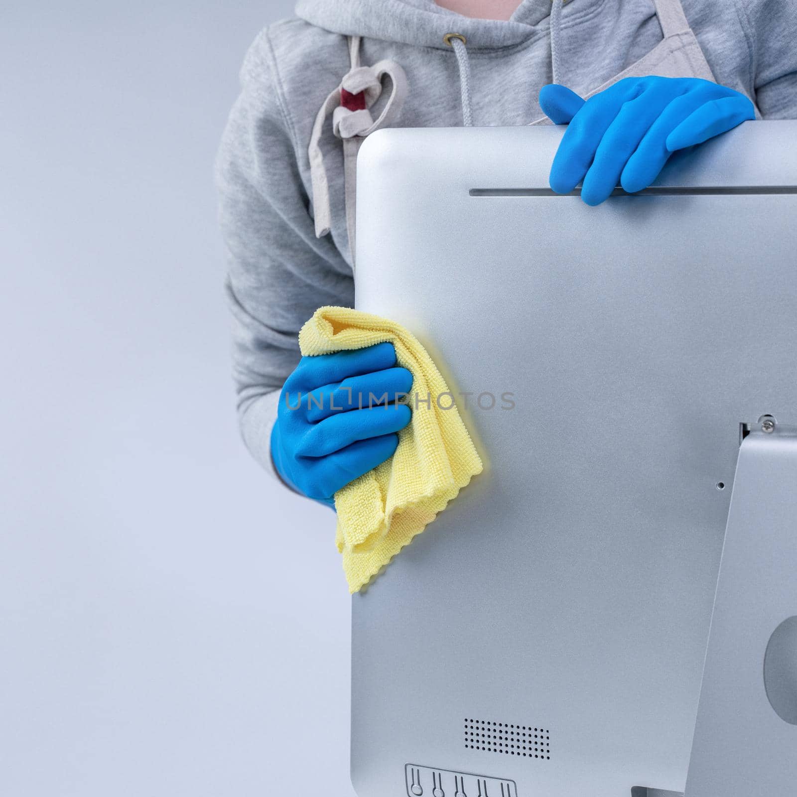 Young woman housekeeper in apron is cleaning silver computer surface with blue gloves, wet yellow rag, close up, copy space, blank design concept. by ROMIXIMAGE