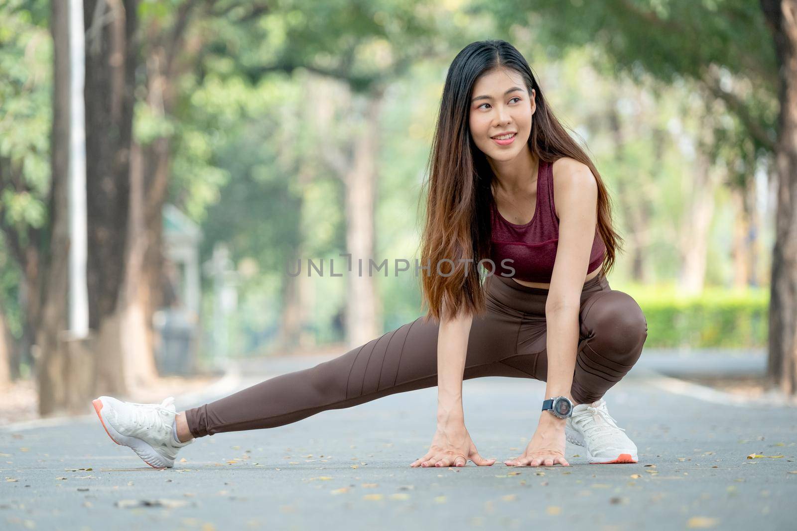Beautiful Asian sport woman stretching right legs on road of park or garden also smile from relaxation after exercise in the morning.
