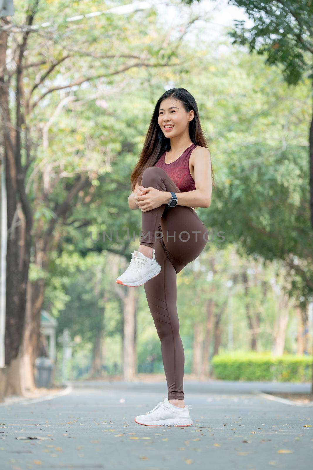 Asian sport woman stand and do one leg raise to practice balance and stretching after exercise in park or garden.