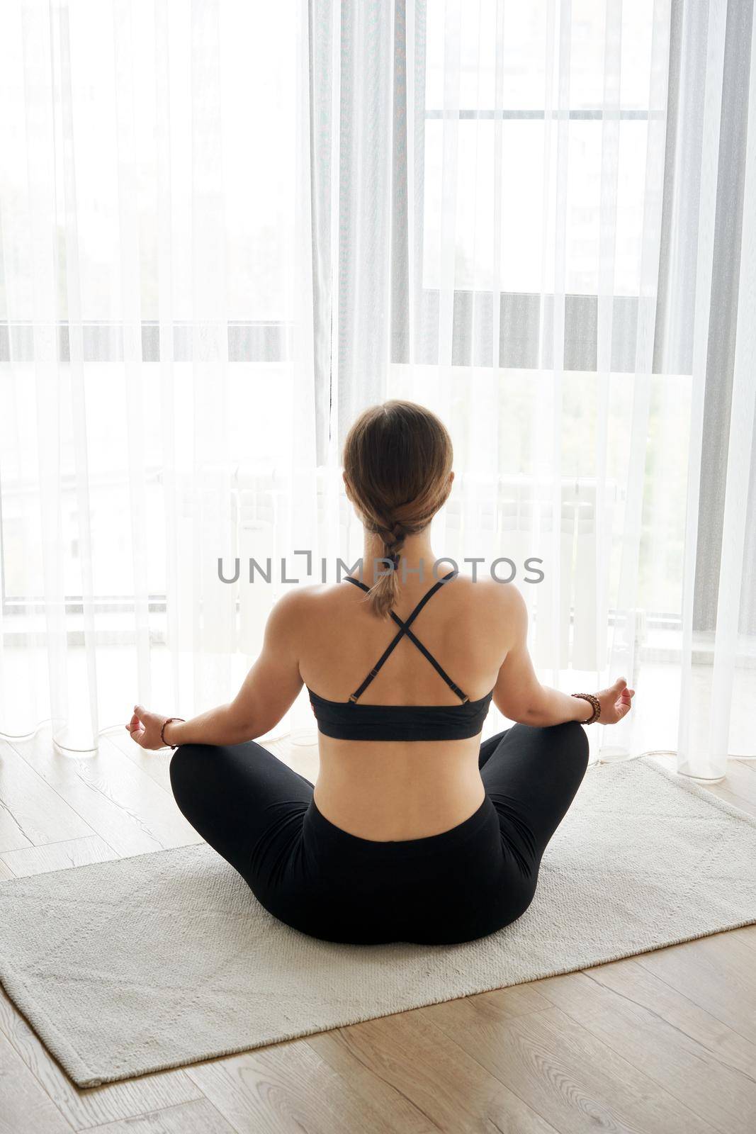 Rear view of girl relaxing in lotus pose at home.Yoga concept by Mariakray