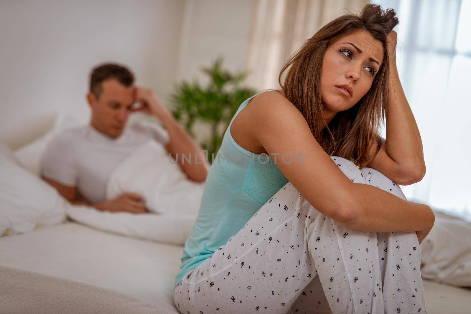 Sad young  woman feels stressed after quarrel with her husband, sits on edge of bed, thinks about something.