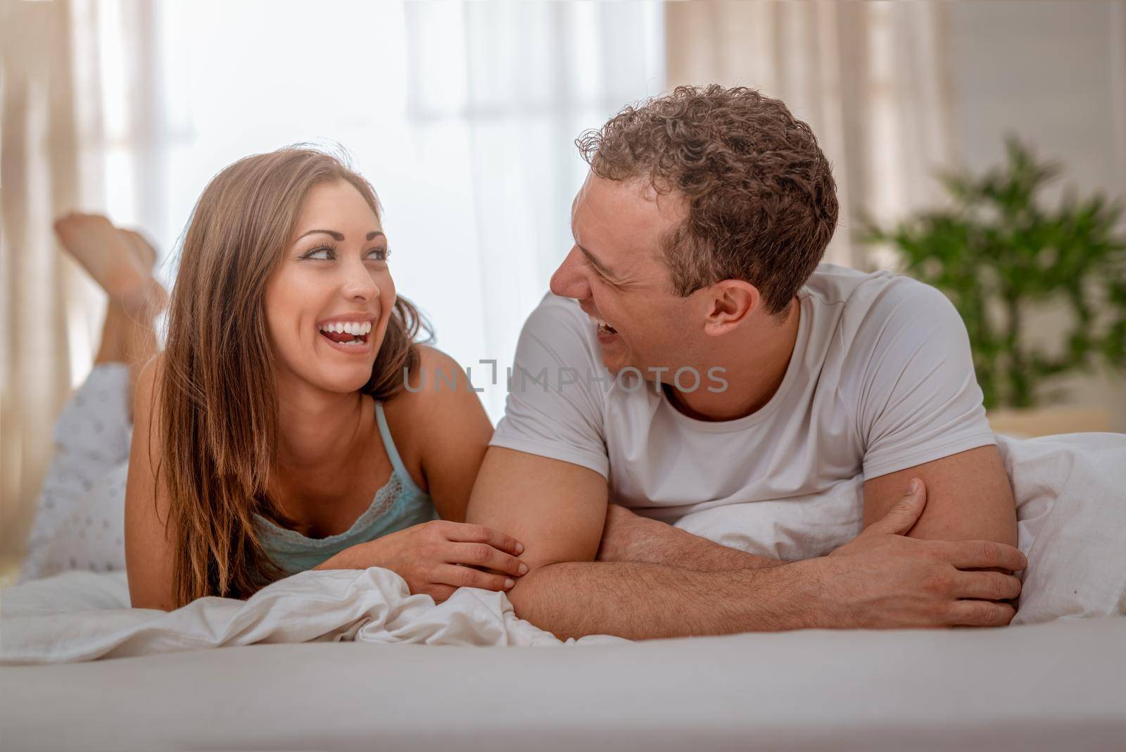Beautiful young loving couple looking each other with love and having lazy morning in bed.