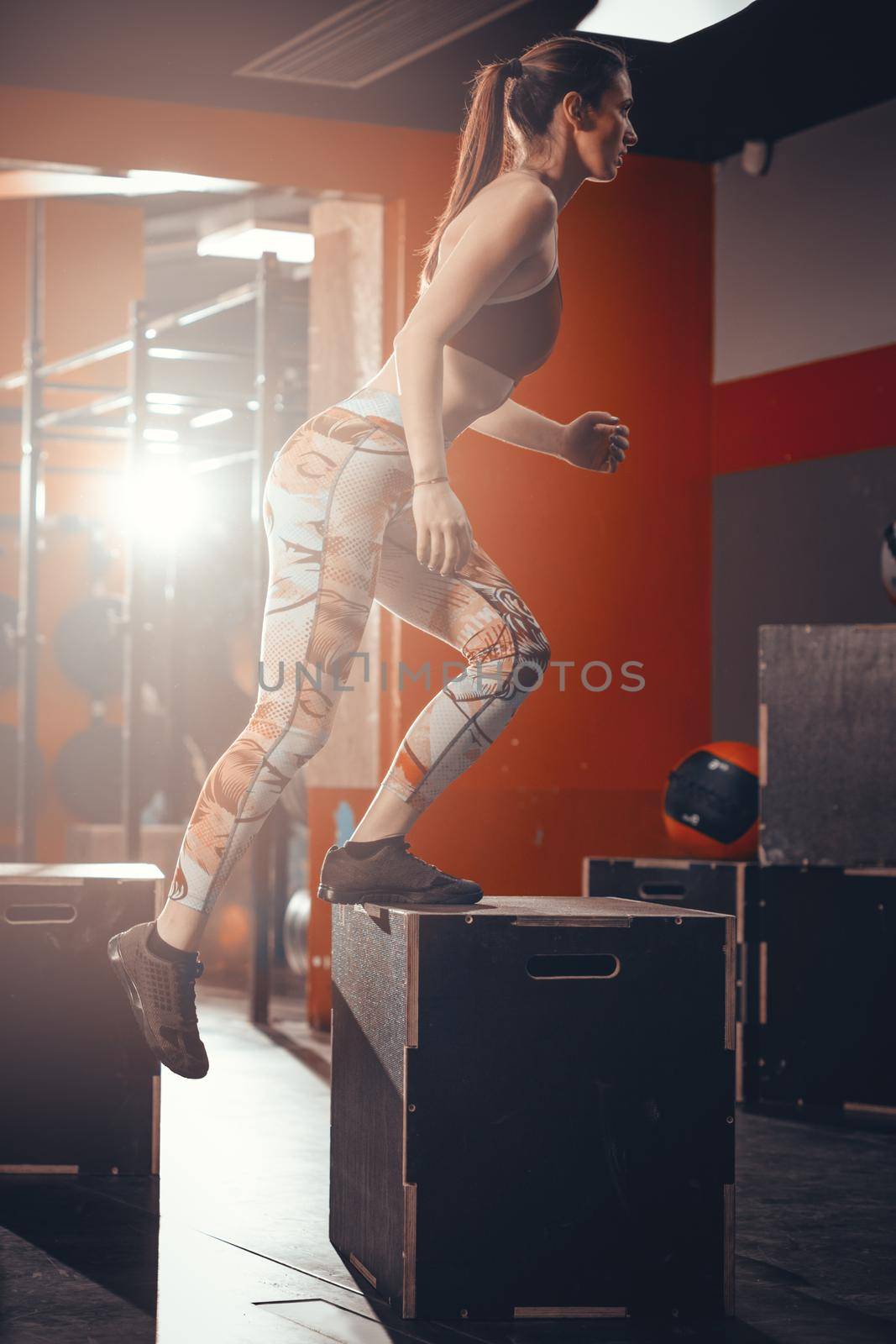 Young fit woman doing hard exercise at the gym. She is jumping on the boxes at the gym.  