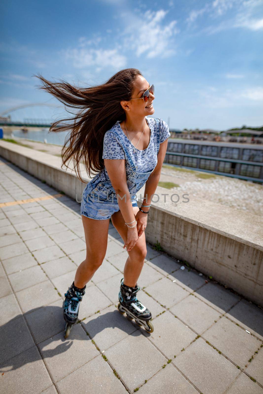 A beautiful smiling young woman having happy time during the roller blanding and enjoying on the city rivershore on a beautiful summer day.