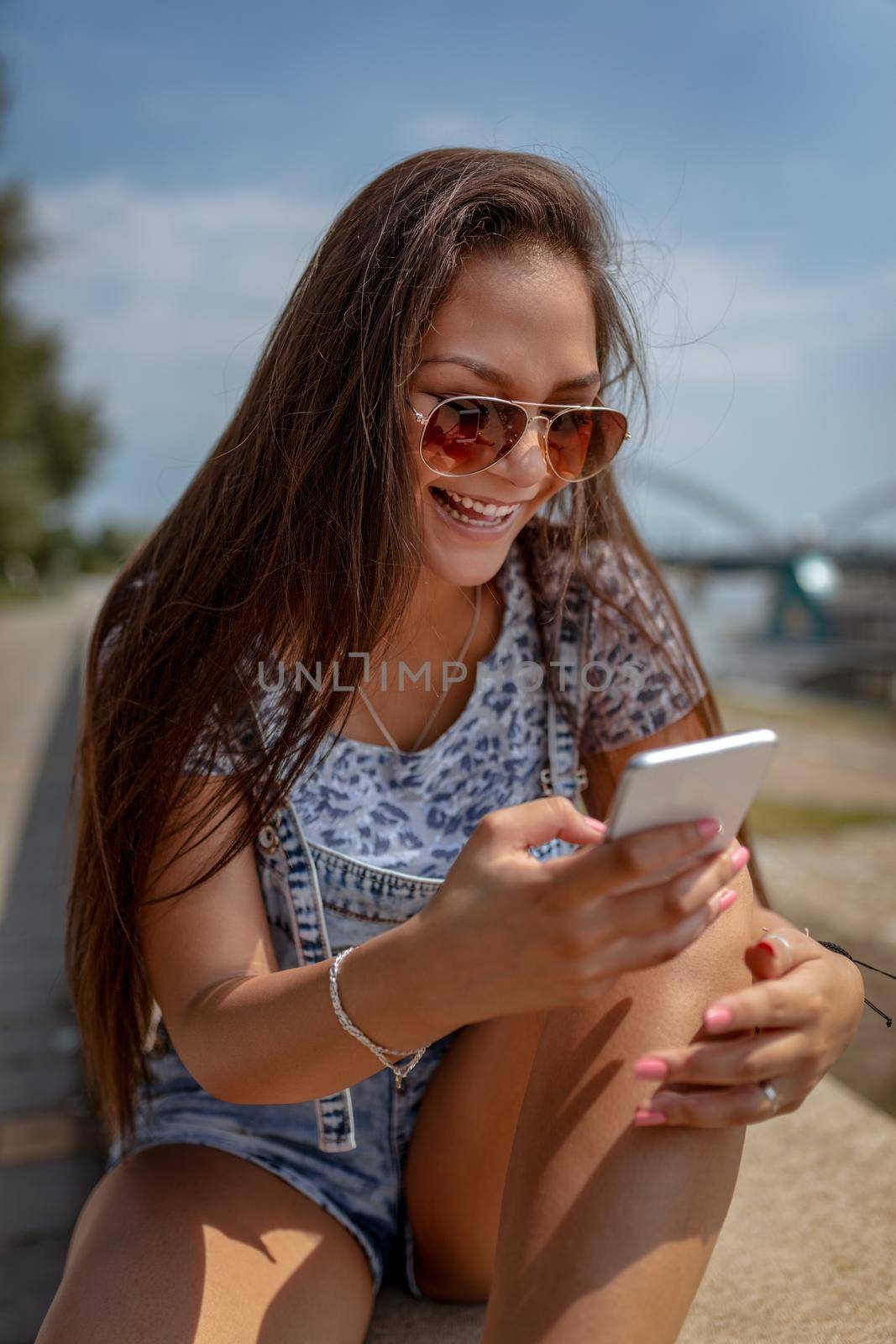 Cute smiling young woman surfing on internet or typing message on smartphone and sharing great news with her friend. 