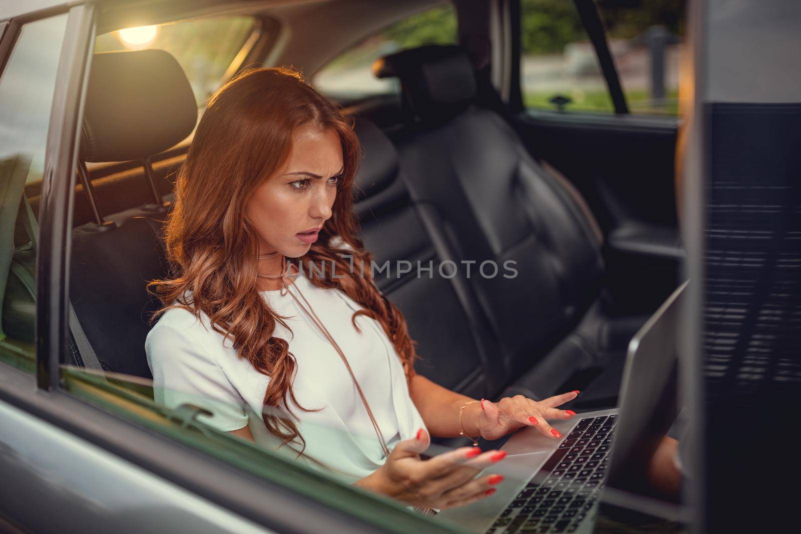 Young confidence business woman typing on her laptop on the back seat in car.