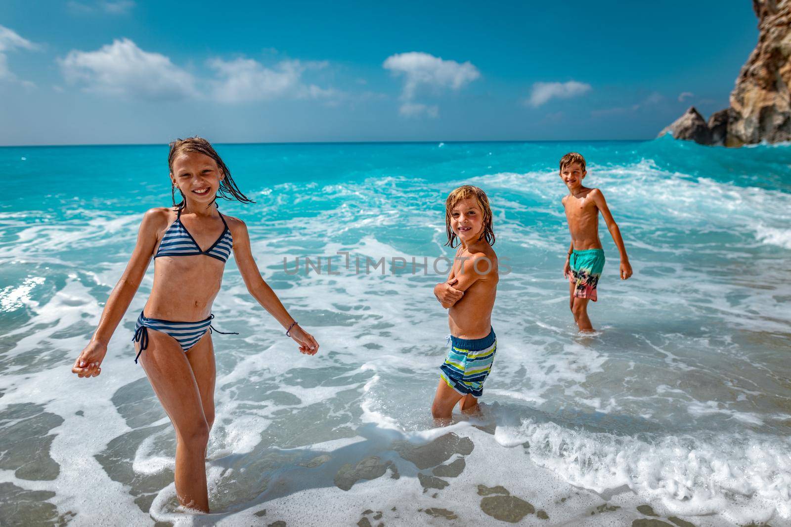 Brothers and sister playing in the shore on the beach during the hot summer vacation day.