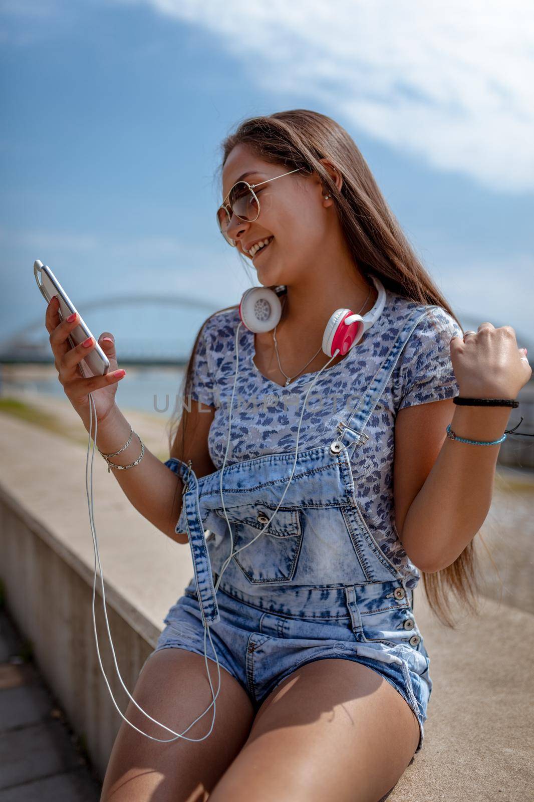 A beautiful smiling young woman texting messages on your mobile phone or using social media and enjoying on the city rivershore on a beautiful summer day. 