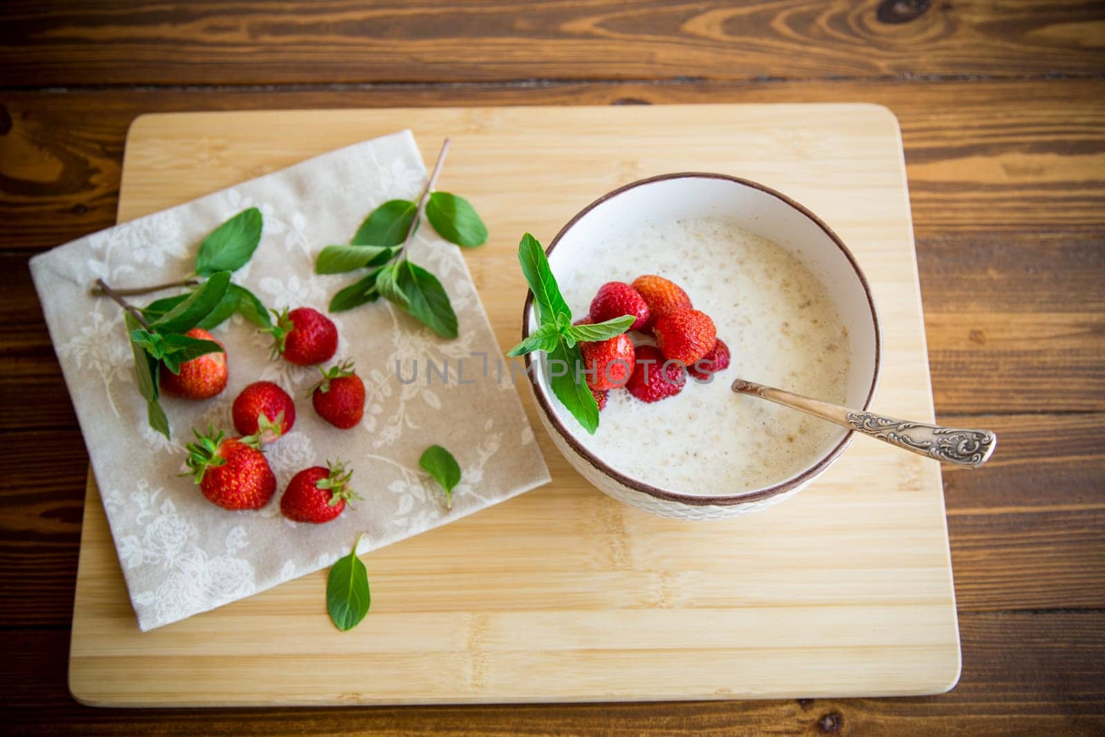 cooked diet oatmeal in a bowl with fresh ripe strawberries, on a wooden table.