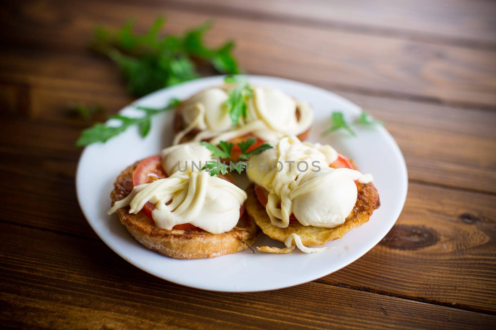 fried in batter sandwiches with tomatoes and mozzarella in a plate with herbs, on a wooden table.