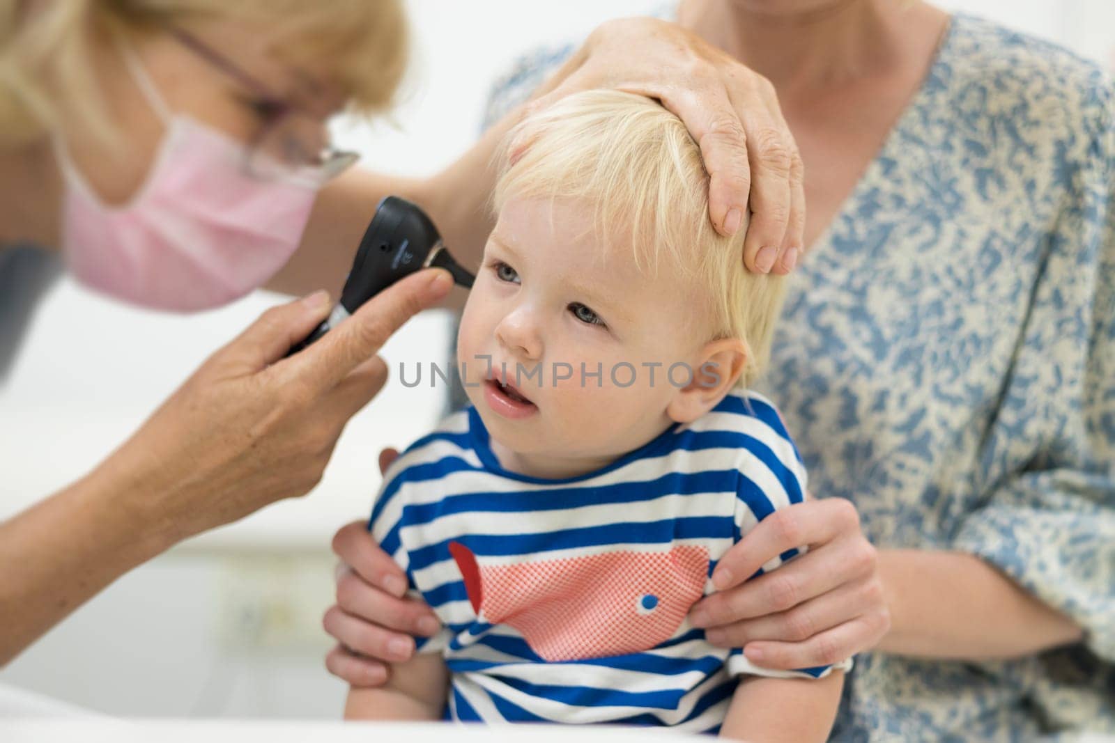 Infant baby boy child being examined by his pediatrician doctor during a standard medical checkup in presence and comfort of his mother. National public health and childs care care koncept