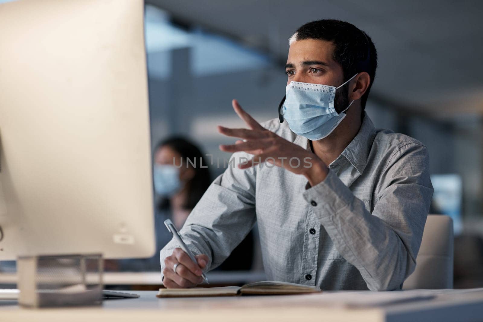 Call center, man and communication with mask at computer while writing notes for advice, customer service and sales. Male telemarketing agent, virus protection and desktop for consulting questions.