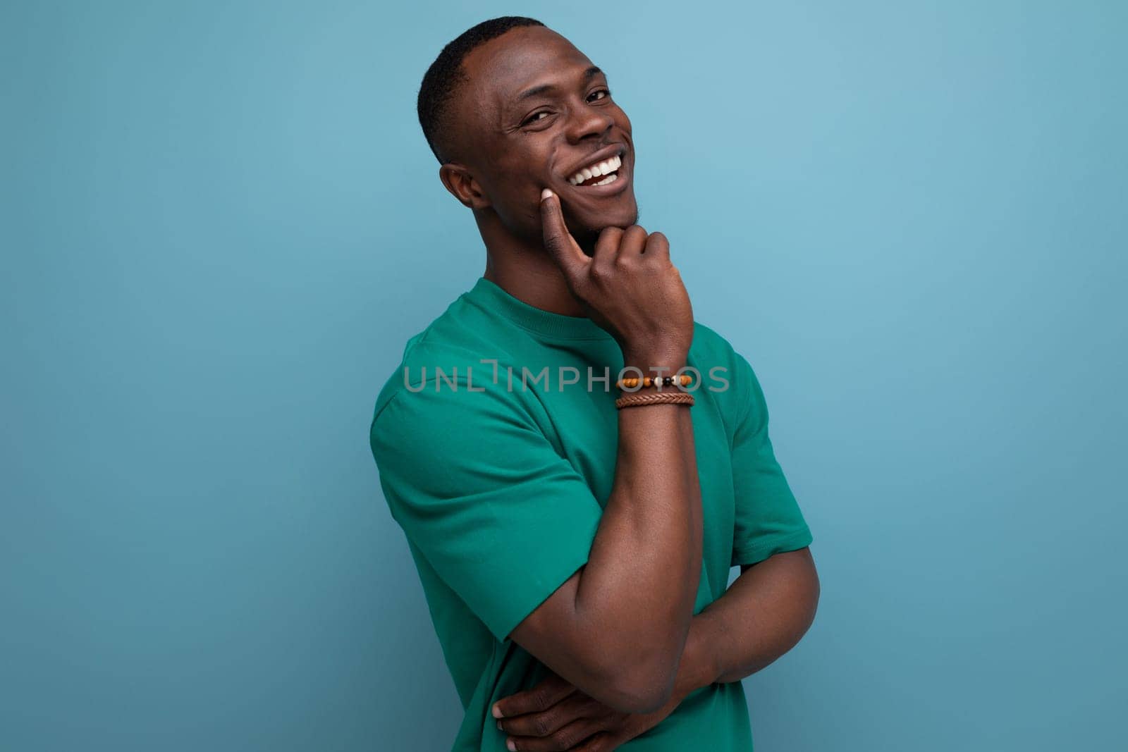 shy young american man in a t-shirt holds his hand to his face on a blue background with copy space. people lifestyle concept.