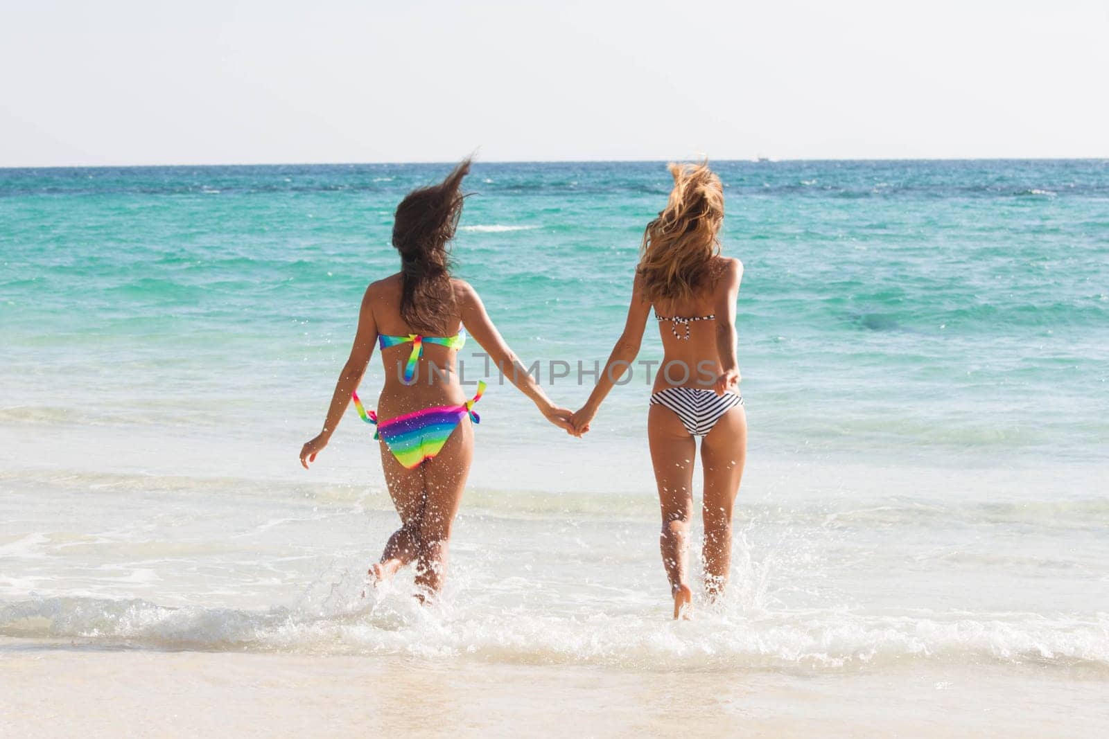 Pretty slim girls at tropical sea beach walking holding hands