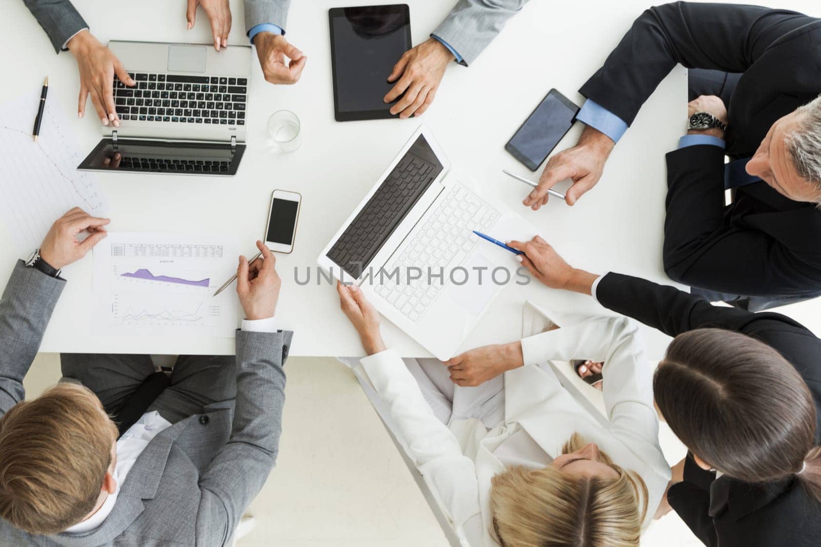 Business people brainstorming at office desk, analyzing financial reports and working with laptops and tablets