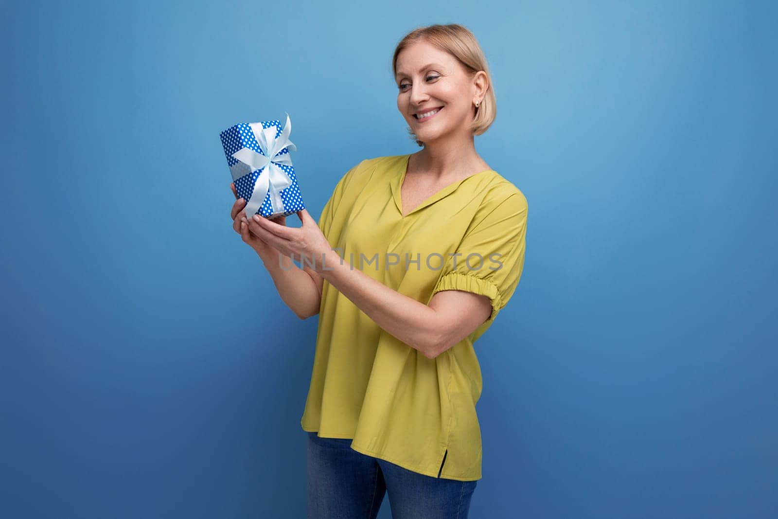 blond middle-aged woman holding a gift box in her hands for the holiday.