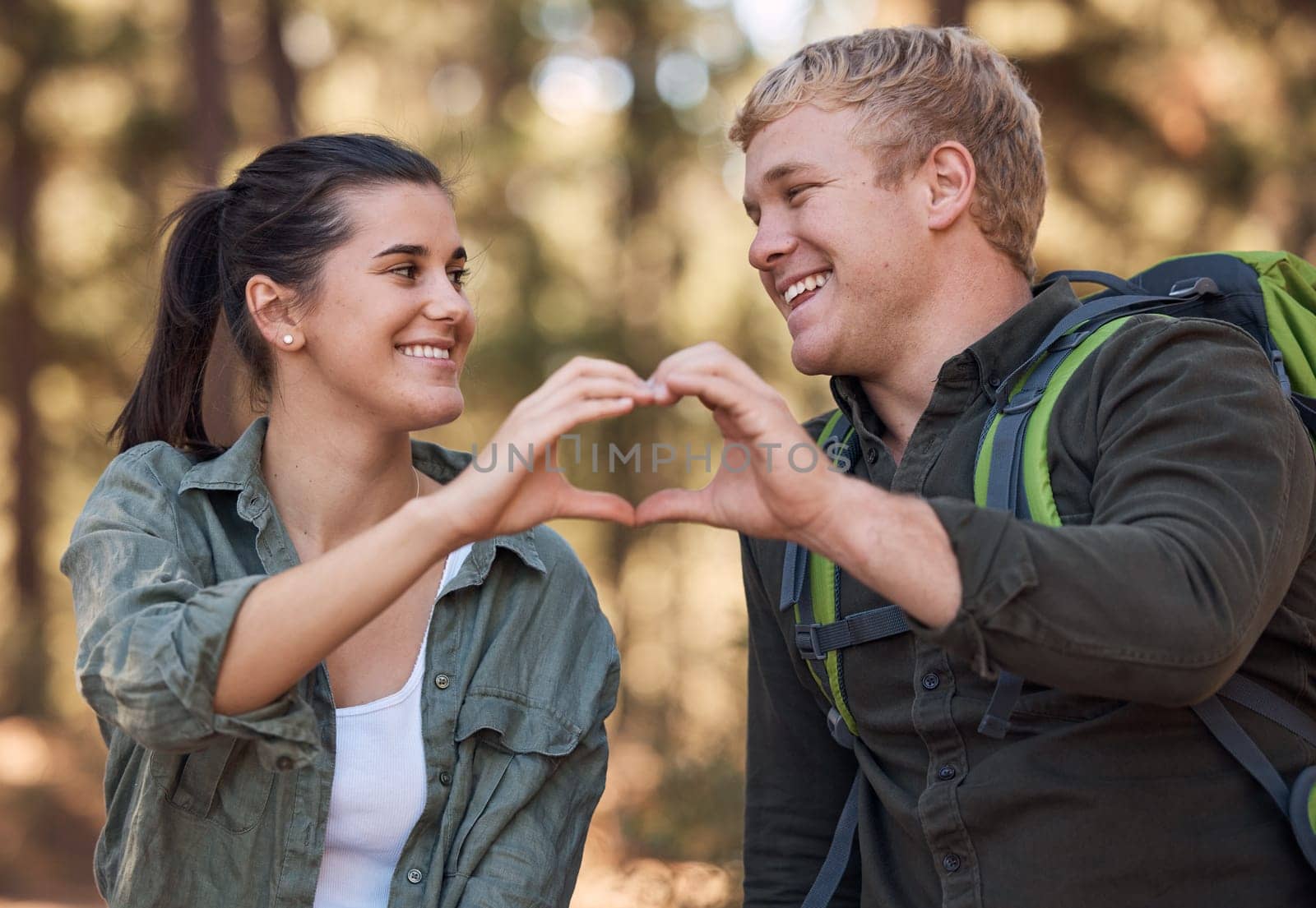 Love, couple and heart hands while hiking in nature for affection or support. Emoji, hand gesture and romance or intimacy shape with happy man and woman on adventure or trekking outdoors in forest