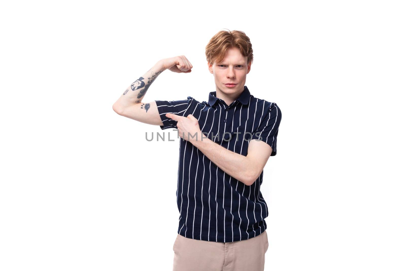confident young European blond guy in a striped polo shirt shows his tattoos on a white background.