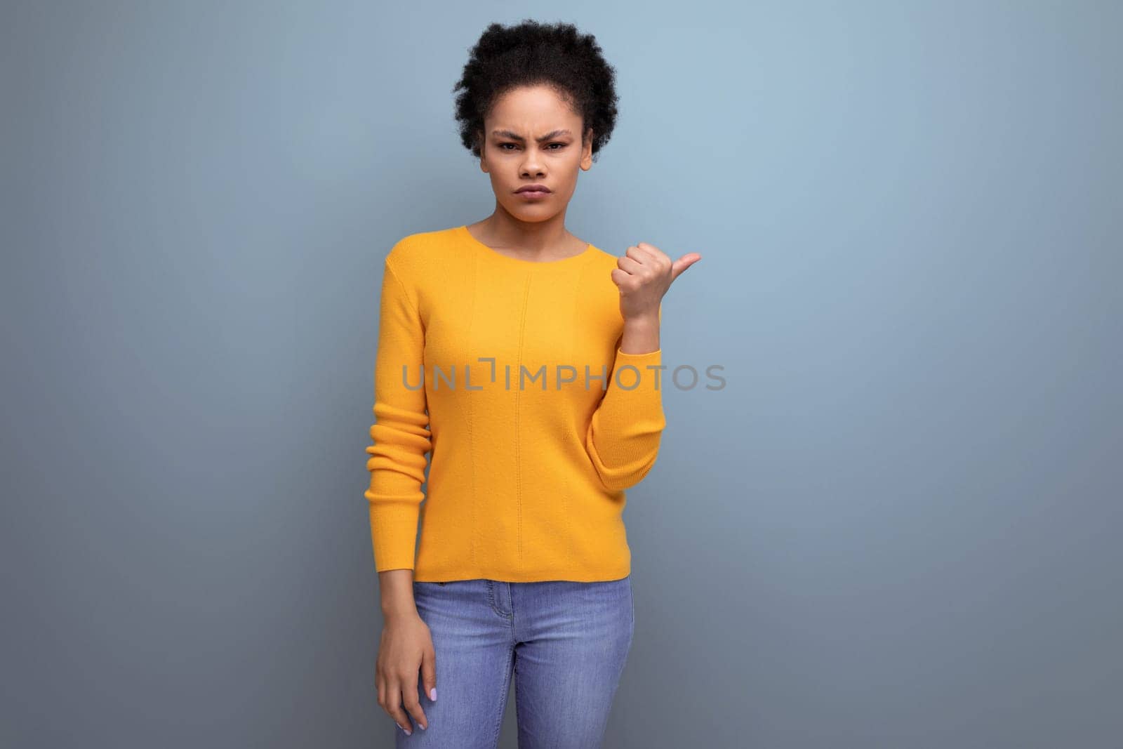 smart young latin woman with afro hair pointing finger to the side on gray background with copy space.